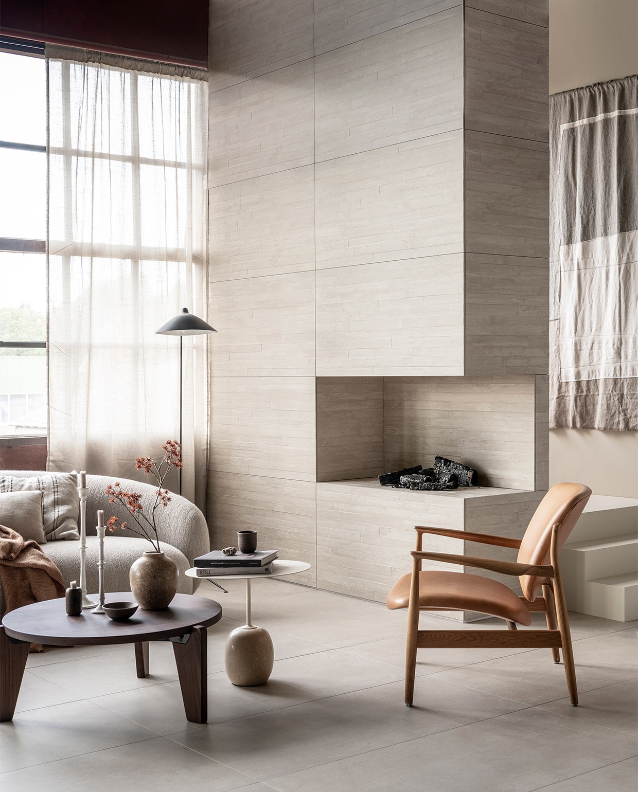 Op de wand: wandtegel Raw Casa Decor 3D in kleur Sand, 60×120 cm, per m² € 69,-. Op de vloer: vloertegel Raw in kleur Sand, 60×120 cm, per m² | M.m.v. justhaasnoot.nl (staande lamp, bank Julep van Tacchini, salontafel Guéridon Bas van van Vitra, witte bijzettafel Lato van &amp;Tradition, fauteuil van hout met leer van House of Finn), zarahome.com (witte metalen kandelaars, stenen vaas), suhka.nl (textielkunstwerk, kom en mok). Overig privébezit. vtwonen 11-2021 | styling Kim van Rossenberg | fotografie Sjoerd Eickmans | productie Tanja Saarberg