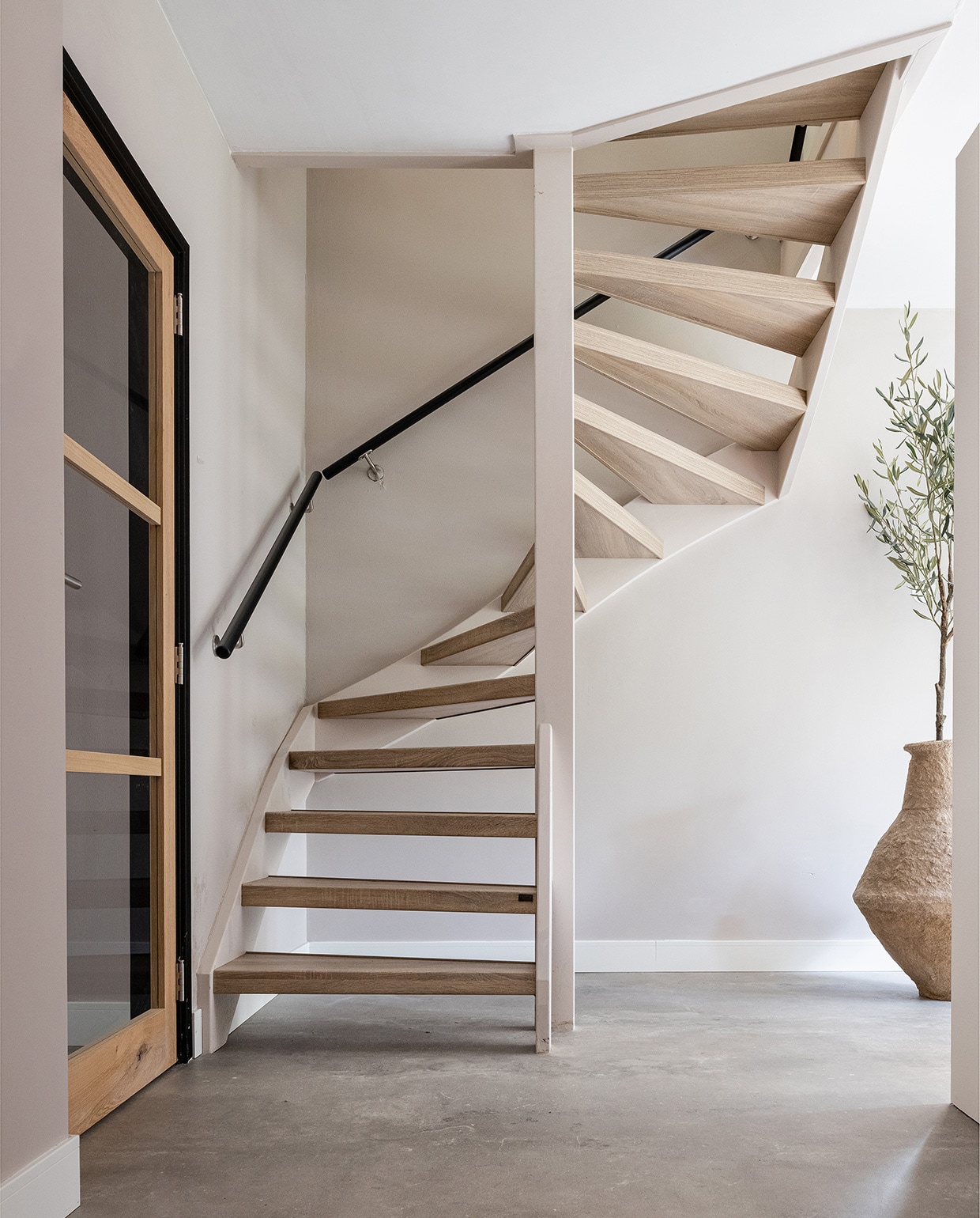Pvc-vloer betonlook Dynamic Cemento 609 met plint, prijs op aanvraag (woninginrichting-aanhuis.nl). Trap bekleed met decor San Diego Oak, prijs op aanvraag, trapleuning rond, kleur Oak, prijs op aanvraag (upstairs.com). Vaas XL € 199,- (eijerkamp.nl). Olijfboom prijs op aanvraag (silk-ka.com). JA | vtwonen weer verliefd op je huis | seizoen 15, aflevering 7| fotografie Sonja Velda