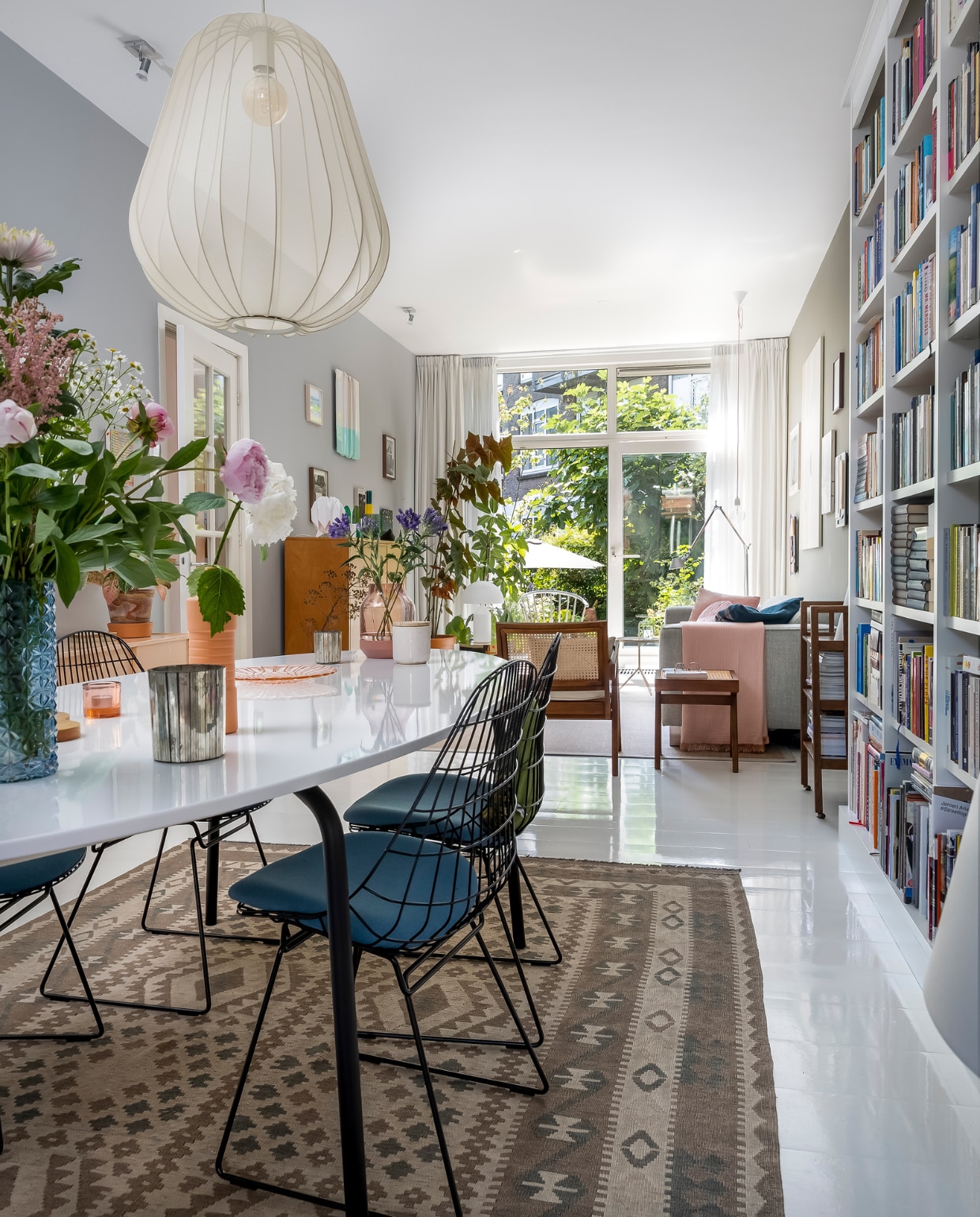 Muurverf Flexa, naam onbekend. Lamp Bolia. Afghaans vloerkleed, herkomst onbekend. Stoelen en houten wandkast Pastoe, eettafel Ikea, blauwe vaas &amp;Klevering, roze vaas Foekje Fleur, sfeerlicht roze Iittala, glazen bord vintage, roze vaas Elevated van Muuto, witte pot geurkaars HKliving. Webbing stoel en bijzettafel Detjer. Boekenkast Lundia. Vloer witte epoxylak over oud parket. Bank Hulshoff, deken Hay, vloerlamp Artemide. Overig herkomst onbekend. vtwonen 10-2022 | fotografie Henny van Belkom