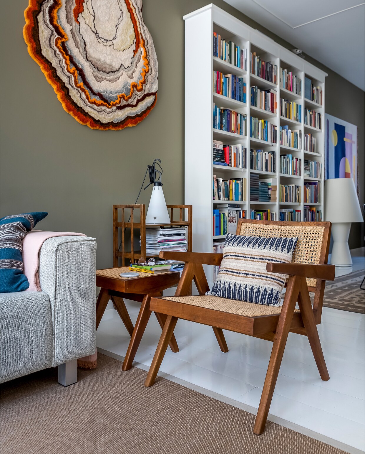 Muurverf Tent van Flexa, wandkleed links Lizan Freijsen, boekenkast Lundia, wandkleed rechts Kukka. Bank Hulshoff, kussens HKliving, deken Hay, lamp links Floss, houten boekentafel onbekend, webbing stoel en bijzettafel Detjer. Lamp rechts de Bijenkorf, merk onbekend. Herkomst Afghaans vloerkleed onbekend, vloer witte epoxylak over oud parket. vtwonen 10-2022 | fotografie Henny van Belkom