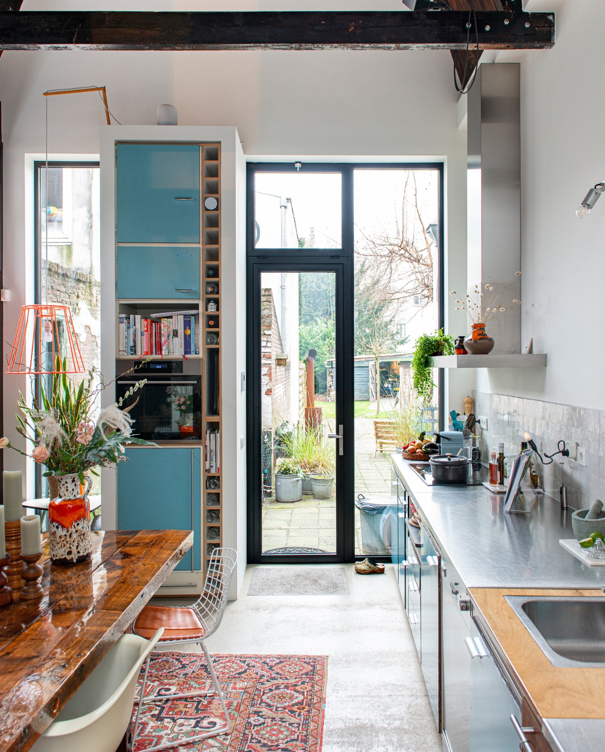 Keuken van Piet Zwart voor Bruynzeel, tafel zelfgemaakt, witte stoel Eames Plastic Armchair voor Vitra, ijzerdraad stoel Wire Chair van Harry Bertoia voor Knoll, spot Nomad van Modular, Perzisch tapijt vintage, hanglamp zelfgemaakt van een oude lampenkap en oranje garen, oven Ikea, houten kandelaars kringloopwinkel, keramieken vaas van de Noordermarkt in Amsterdam. Overig onbekend. productie De Binnenkijkers | styling Jeske Weel | fotografie Caroline Coehorst