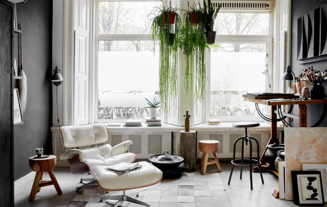 Het atelier in de voorkamer met lounge chair en ottoman van Eames voor Vitra. Tekentafel, krukken en slagersrek Marktplaats. Lamp Serge Mouille. Leren karpet overgenomen van een vriend. Mand uit Marokko. Sokkel van een markt, de vaas erop is een reissouvenir. vtwonen 2-2020 | fotografie Wilma Custers/features &amp; more | tekst Chris Muyres