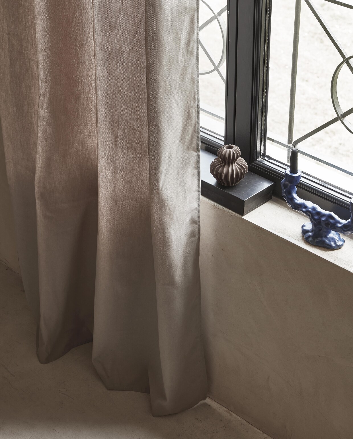 Taupe gordijn Denim Flax, lichtdoorlatend, met ring, 270×140 cm (hxb) € 55,99M.m.v. vtwonen.nl (blauwe kandelaar van Ferm Living), hm.com/home (bruin aardewerken vaasje), zarahome.com (zwart stalen kistje). NEE | vtwonen 11-2022 | Productie Tanja Saarberg | Styling Sanne Ketelaar | Fotografie Peggy Janssen