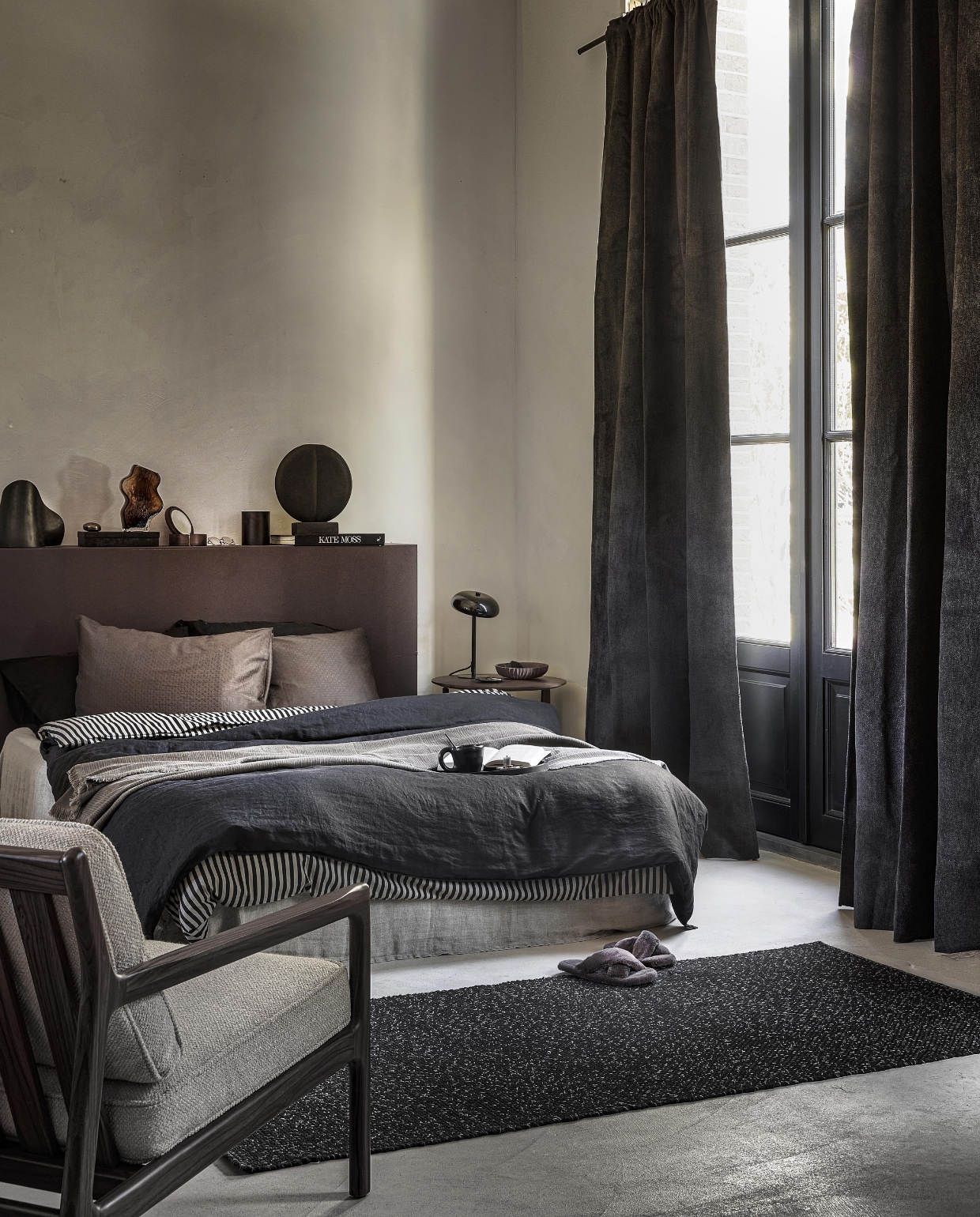 Antraciet gordijn Snow, verduisterend, met plooi, 270×140 cm (hxb) € 64,99M.m.v vanbinnen.com (fauteuil, bijzettafel), hm.com/home (linnen dekbedovertrek, dekbedovertrek met streep, organische bruine vaas, houten spiegel, bruine aardewerken schaal), zarahome.com (linnen onderlaken, pantoffels, metalen doos, geurkaars, zwarte tafellamp), homestede.nl (metalen organische tafellamp, rond sculptuur). Overig privébezit. vtwonen 11-2022 | Styling Sanne Ketelaar | Fotografie Peggy Janssen
