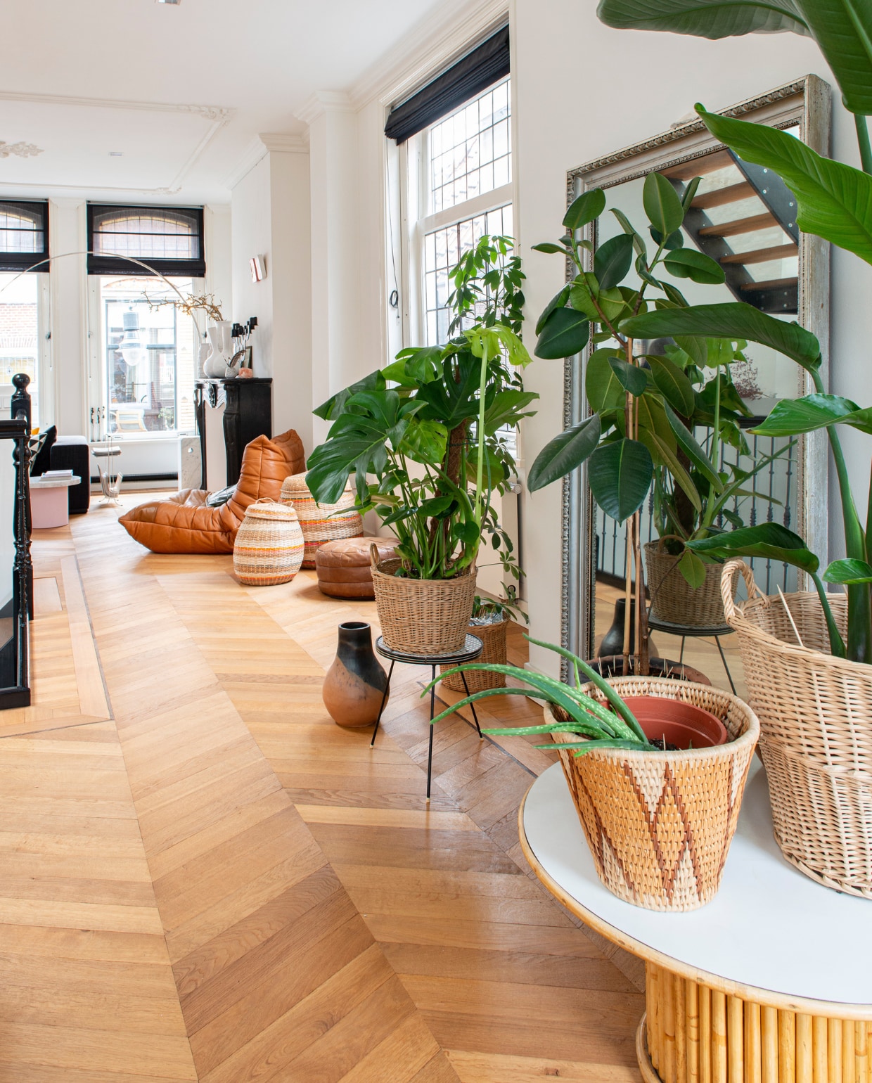 Rotan tafel, manden, plantenpotten, plantentafel en poef via kringloopwinkel en rommelmarkten, vaas op vloer gemaakt door oma. vtwonen 10-2022 | productie De Binnenkijkers | styling Jeske Weel | fotografie Caroline Coehorst