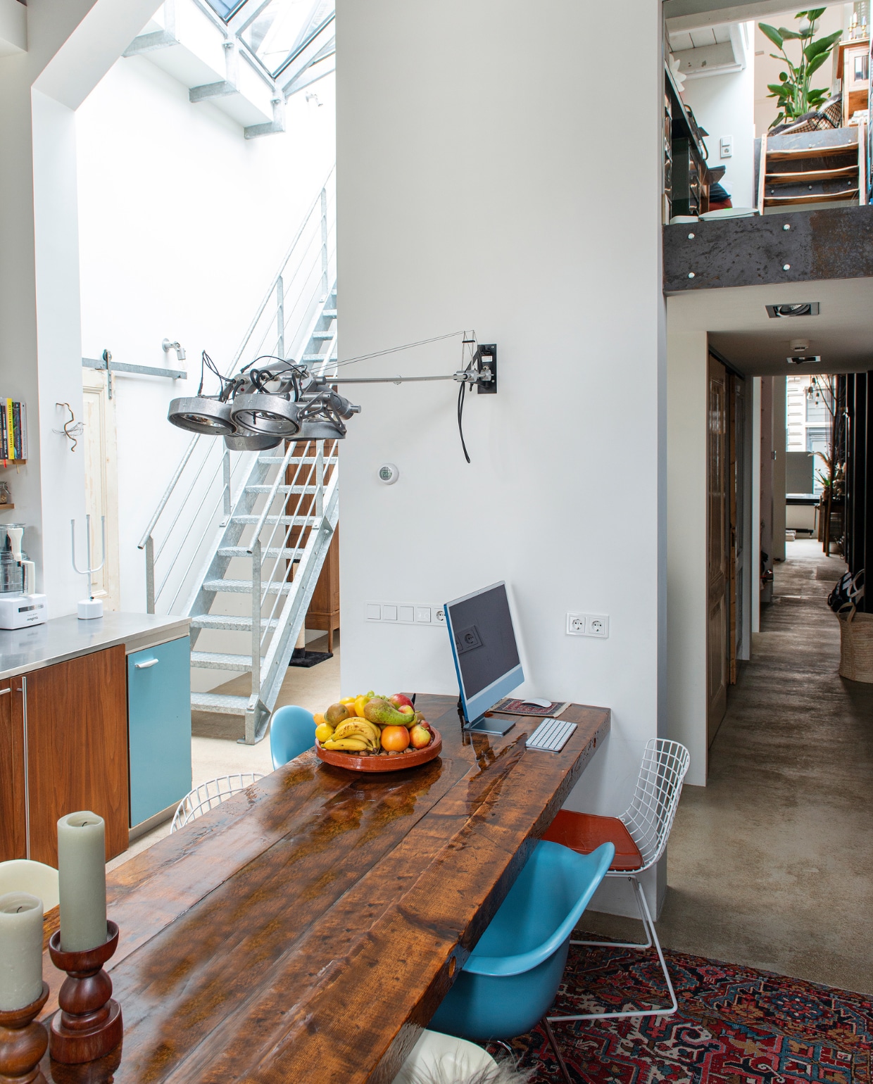 Tafel zelfgemaakt van oude balken en behandeld met epoxy, witte en blauwe stoelen stoel Eames Plastic Armchair van Vitra, stoel ijzerdraad Wire Chairs van Harry Bertoia voor Knoll, lampen boven tafel en in gang Nomad van Modular, Perzisch tapijt vintage, driearmige kandelaar Flames van Chris Kabel voor Droog, houten kandelaar en fruitschaal kringloopwinkel. vtwonen 10-2022 | productie De Binnenkijkers | styling Jeske Weel | fotografie Caroline Coehorst