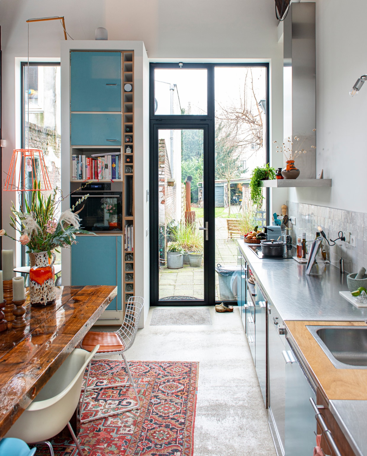 Keuken van Piet Zwart voor Bruynzeel, tafel zelfgemaakt, witte stoel Eames Plastic Armchair Vitra, ijzerdraad stoel Wire Chair van Harry Bertoia voor Knoll, spot Nomad van Modular, Perzisch tapijt vintage, hanglamp zelfgemaakt van een oude lampenkap en oranje garen, oven Ikea, houten kandelaars kringloopwinkel, keramieken vaas van de Noordermarkt in Amsterdam. Overig onbekend. vtwonen 10-2022 | Productie De Binnenkijkers | Styling Jeske Weel | Fotografie Caroline Coehorst | Tekst Chris Muyres