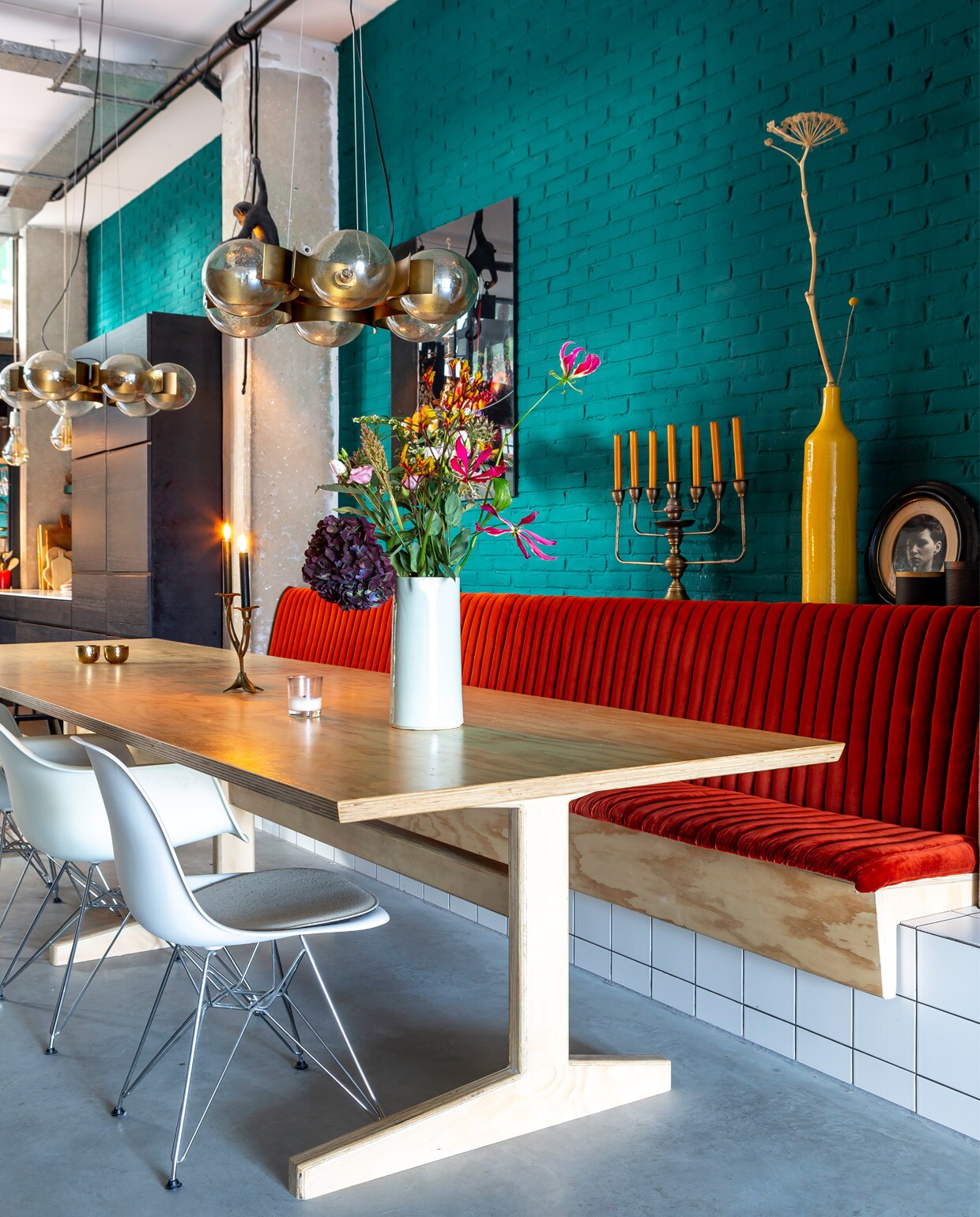 Tafel en bank op maat gemaakt door de vorige bewoner. Stoelen Vitra Eames DAR (met) en DSW (zonder armleuningen). Glazen bollampen Allis van Soho Home. Muurprint van een stilleven door Kevin Best, lamp Monkey van Seletti. Kandelaar op tafel van OU. Boutique Stories. Kan van Anders Nog Iets. Zevenarmige kandelaar Homestock, handgemaakte gele vaas vintage. Kast op maat gemaakt en geschilderd in de kleur van de muur: Mid Azura Green 96 van Little Greene. vtwonen 10-2020 | Fotografie Henny van Belkom | Tekst Renske Schriemer