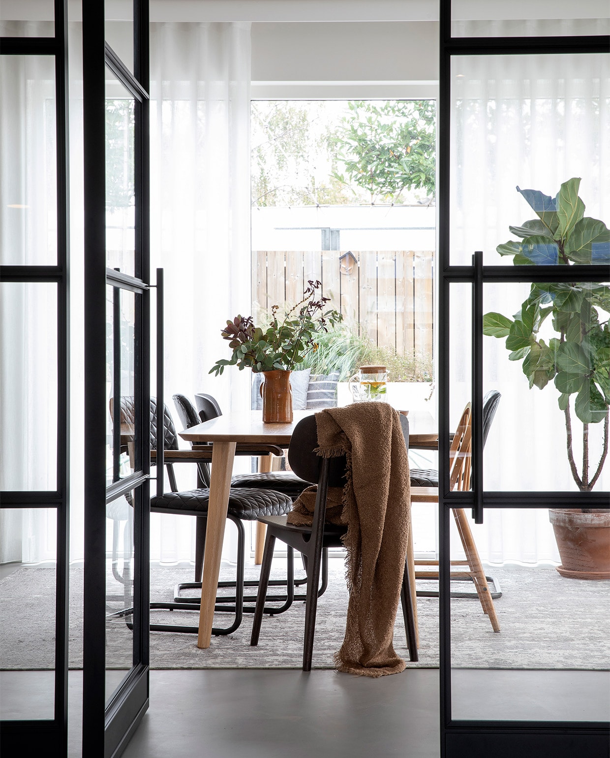 Deuren met stalen kozijn op maat gemaakt door Wout Jansen. Tafel Sav &amp; Økse. Stoelen By-Hoo. Hoge kinderstoel Ikea via Marktplaats. Vloerkleed Floorpassion. Plaid H&amp;M Home. Vaas van de kringloopwinkel. vtwonen 08-2021 | fotografie Macha Gutlich