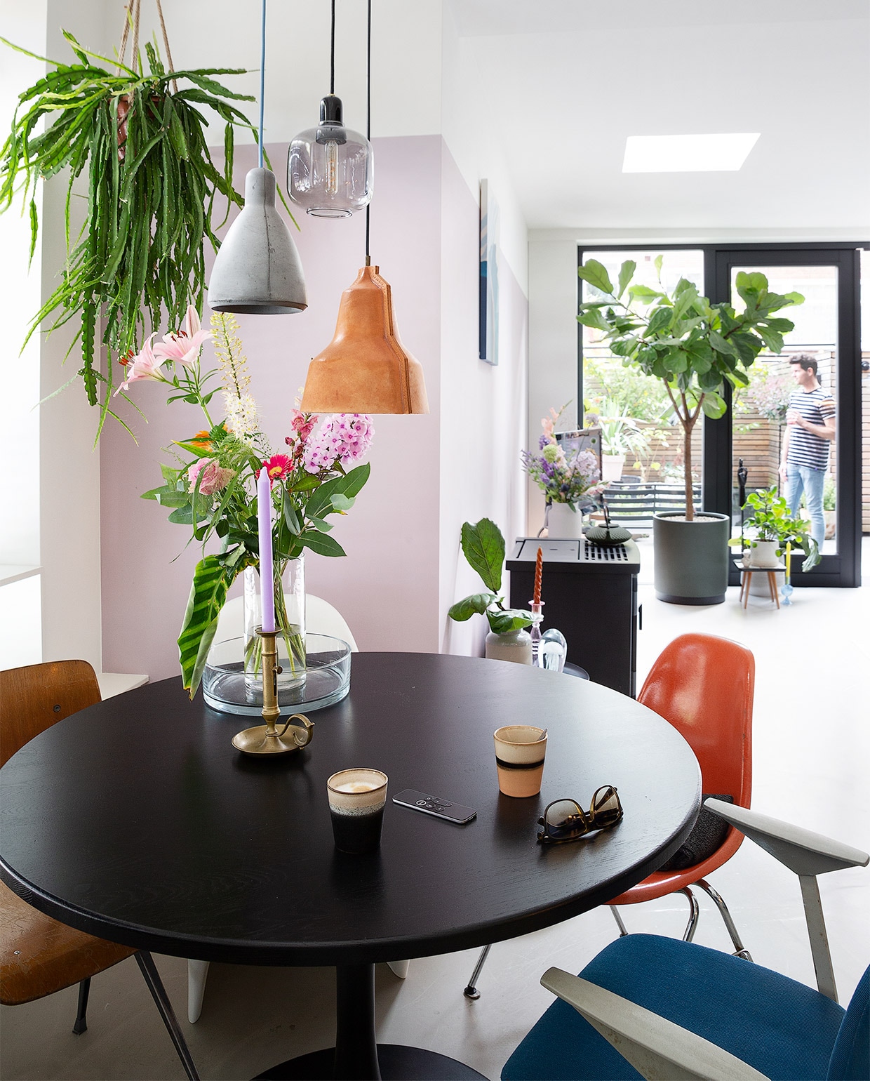Hangplant Intratuin, hanglampen van links naar rechts Seen Design, Normann Copenhagen, Puik Design. Tafel Woood, houten stoel, oranje stoel, blauwe stoel De Machinekamer, witte stoel Verner Panton. Vaas Bloomon, fruitschaal Kwantum, kandelaar, lage tafel familiestuk, mokken HKliving. Pelletkachel Nordic Fire, witte vaas Hema, glazen kandelaar met rode kaars Sissy-Boy, ornament kwal Bijenkorf, zwarte theepot Bredemeijer, witte vaas Bloomon. Grote groene bloempot 123planten, lage tafel Vestbjerg Jens, witte bloempot D&amp;M deco. NEE  | vtwonen binnenkijken special 2021 | Fotografie Jansje Klazinga | Styling Roy Seen