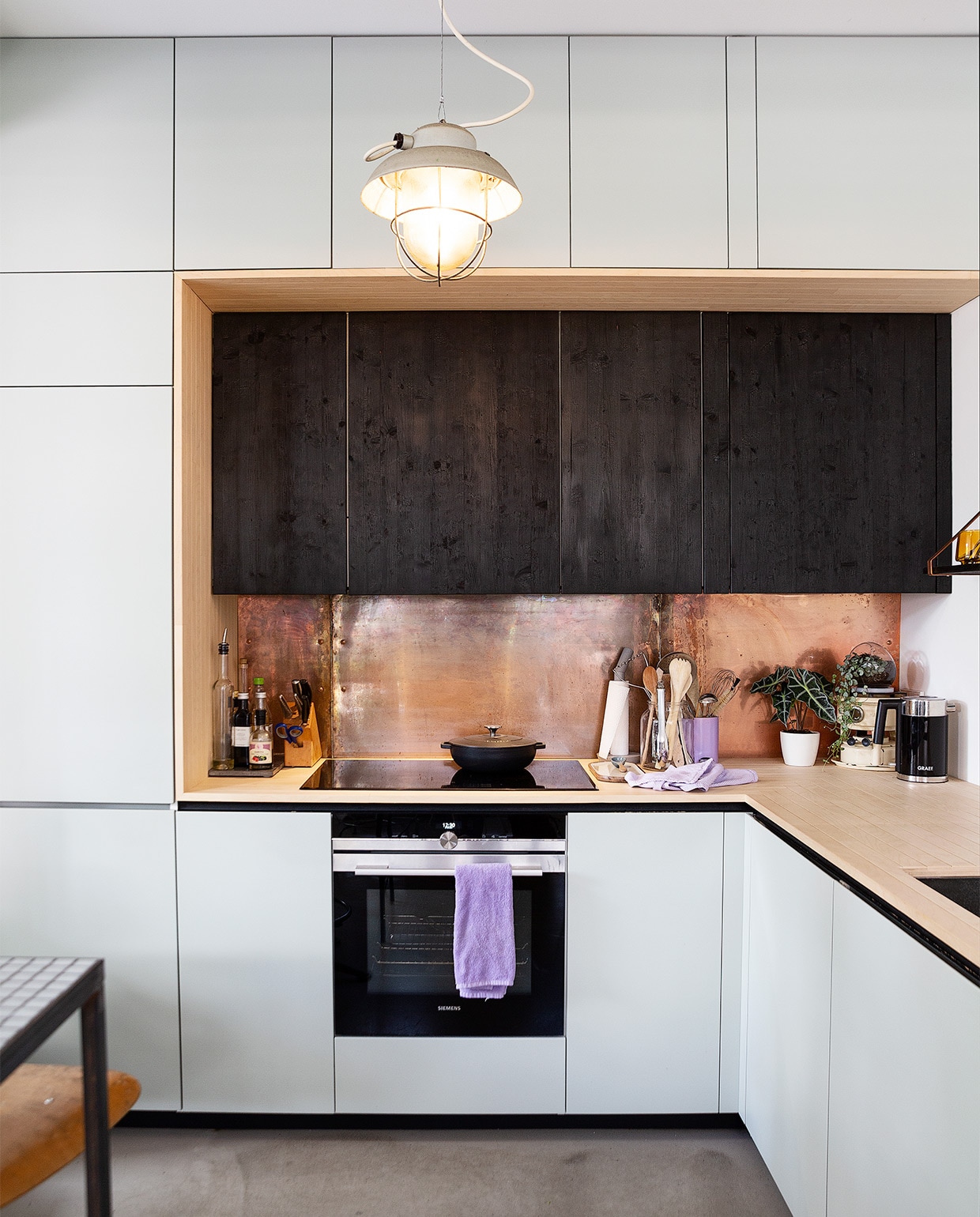 Keuken Ikea met zelfgemaakte fronten van opmaatzagen.nl. Groen op muur Mizzle Farrow &amp; Ball, kleur zwart zelfgemaakt met behulp van een gasbrander en gekookte lijnzaadolie. Aanrechtblad berkenmultiplex behandeld met lak van Skylt, koperen plaat plaatopmaatwinkel.nl. Hanglamp Brocantiek de Linde, wandlamp Zangra. Hoge tafel zelfgemaakt, barkruk met leuning, kruk De Machinekamer. Messenblok, mes Zwilling, steelpan Sigg, keukenrolhouder, keukenschaar Hay, glazen pot Van Dijk &amp; Ko, lila pot, glazen bloempotje, weegschaal Dille &amp; Kamille, lila theedoek Sissy-Boy, wit bloempotje Ikea, petroleumstel familiestuk, waterkoker Graef, snijplank H&amp;M Home. Zeeppompje Tiger, witte borden Iittala, vintage bestekcassette Marktplaats, schaal van kurk uit Lissabon. Oranje theeglazen Jysk, potje met deksel Kwantum, groene glazen Iittala, karaf Vij5, vintage laboratoriumglazen Van Dijk &amp; Ko, schaaltjes, snijplank, zwarte kandelaar, ijzeren plantentafel Sissy-Boy, melkkan kringloop. Keukenschaar Hay, witte kreeft Pols Potten, glazen vaas Bloomon, houten bestek decoratiemateriaal Hudson’s Bay, groene pot Loods5, blauwe vogel museumshop Guggenheim, glazen schaal familiestuk. Kaars Søstrene Grene, mokken HK Living, groene koffiekan, keukenklok familiestuk, grijze bloempot Ikea, schaal Intratuin. Stenen bloempot Casa, verf op balk Hensotherm 410KS. NEE  | vtwonen binnenkijken special 2021 | Fotografie Jansje Klazinga | Styling Roy Seen