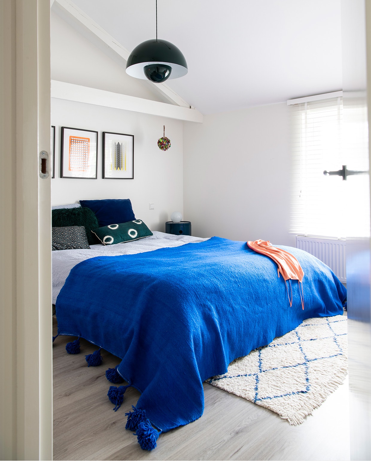 Bed Made. Blauwe sprei en vloerkleed The Souks. Hanglamp Verner Panton &amp;Tradition. Nachtkastje Kartell. Kunstwerk Risoprints Sigrid Calon. Blauw kussen Kvadrat/Raf Simons. Beddengoed Hema. Groen kussen onbekend. NEE | vtwonen binnenkijken special 2021 | productie Insidehomepage | styling Kim Timmerman | fotografie Louis Lemaire