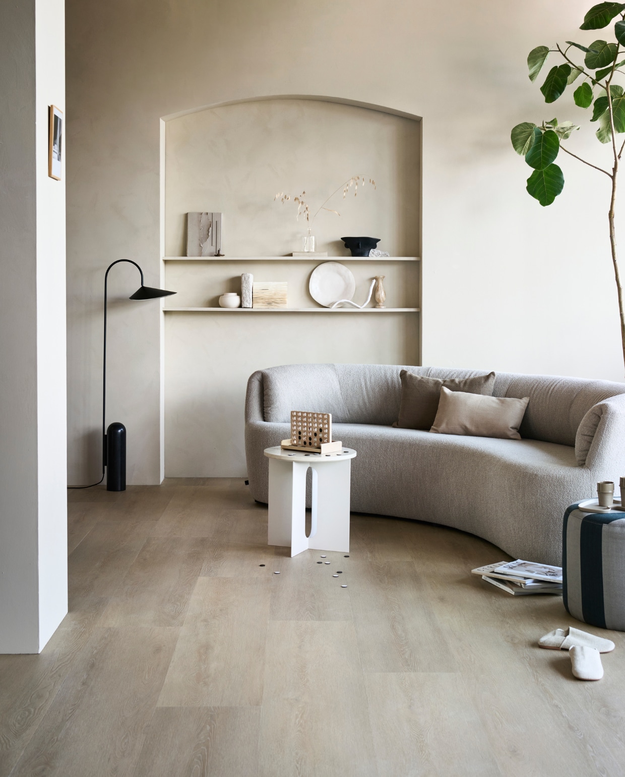 pvc-vloer Wide Board, kleur Naturel, 152,5×30,5 cm, dryback per m² € 45,95, click per m² € 67,95.M.m.v. pure-original.nl (muurverf Fresco in kleur Old Linnen), fest.amsterdam.nl (bank), vtwonen.nl (vloerlamp van Ferm Living), designtales.nl (bijzettafel), homestede.nl (fauteuil), instagram.com/ansdekruyf (schilderij), sofacompany.com (gestreepte poef), hmhome.com (zwarte vaas, keramisch potje, dienblad), zarahome.com (glazen vaasje, bord, spel, pantoffels, kussens), sissy-boy.com (mok). Overig privébezit. vtwonen 10-2022 | productie Tanja Saarberg  | styling Sanne Ketelaar | fotografie Sjoerd Eickmans