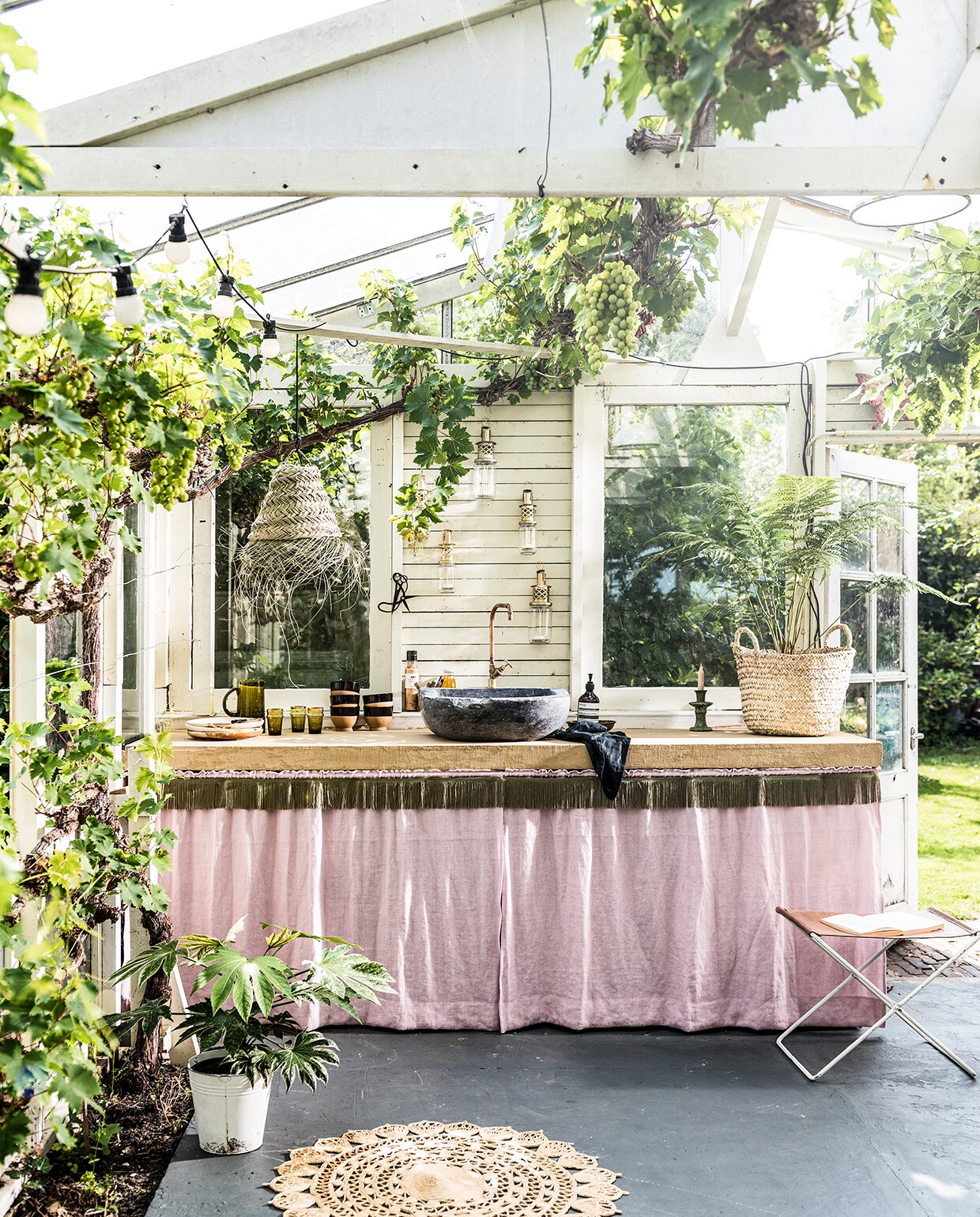 Franjeband in legergroen (aboeken.nl). Lichtroze linnen stof Brera Lino Pale Rose F1723/40 van Designers Guild (wva.nl). Aanrechtblad voorzien van beton ciré in de kleur Amarillo Miel (betoncirenederland.nl). Natuurstenen gootsteen met koperen kraan (oudebouwmaterialen.nl). Grote mand Essaouira Fishermen Basket, maat M, lampenkap Essaouira Triangle Closed, maat S, groene glazen Trad Mor, hoogte 12 cm, groene karaf, lantaarns, groene kandelaar uit de Tamegroute serie (householdhardware.nl). Kommen van keramiek met zwarte rand, grote borden (hkliving.nl). Handzeep Aesop (skins.nl). Fles zout, dressing Nicolas Vahé (societyoflifestyle.com). Grijze doek (hm.com). Overig privébezit. vtwonen tuin special 2 2020