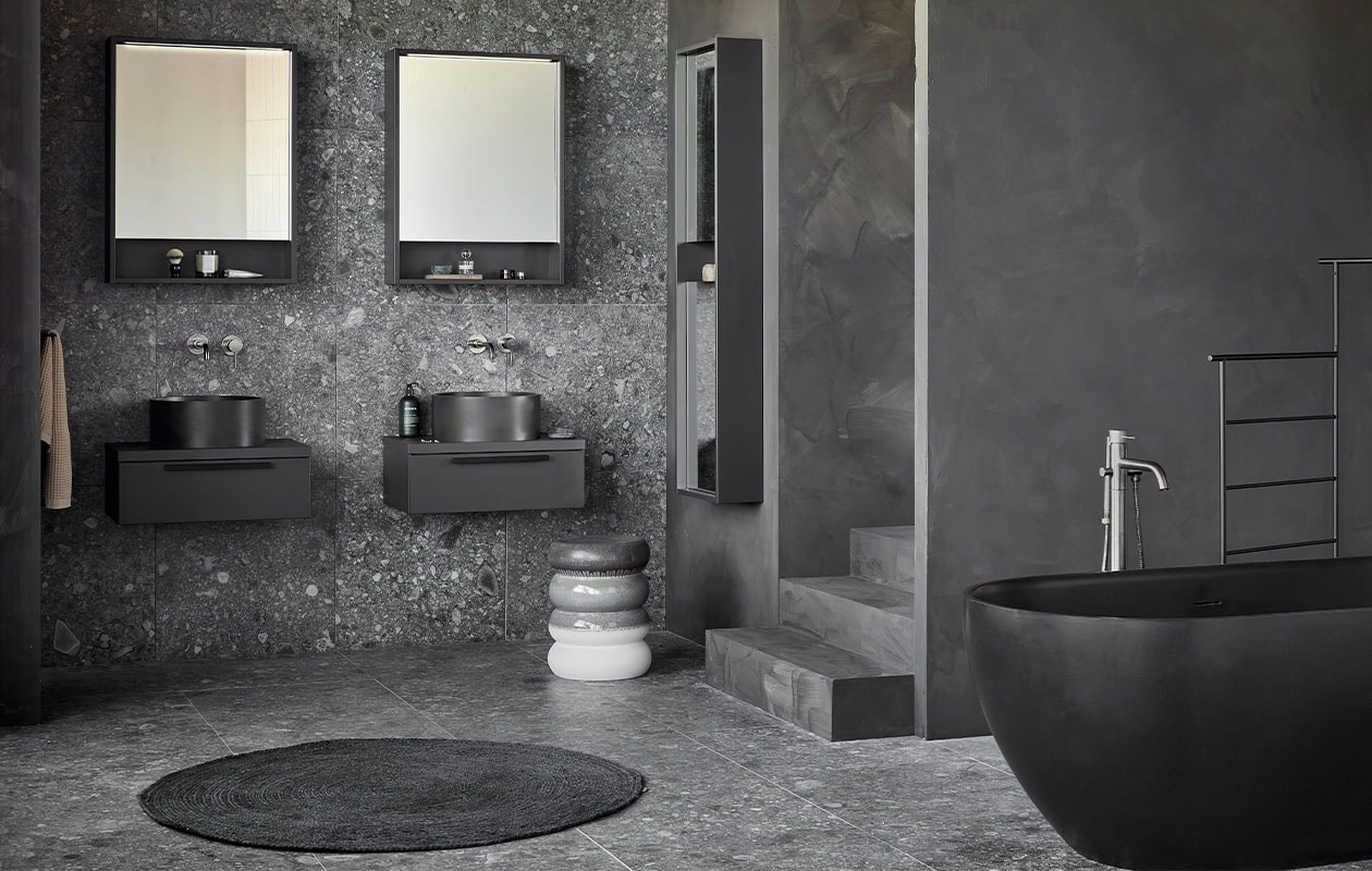 Kunststof spiegelkasten Handy Beauty in zwart, inclusief ledstrip met bewegingssensor, 59,6x60x10 cm (lxbxd) (ook verkrijgbaar in breedtematen 90 cm en 120 cm en in wit, zand en grijs). Quartz waskommen Circle in zwart, 37×15 cm (Øxh) (ook verkrijgbaar in grijs en in Top Solid en Marmer). Kunststof afdekblad in matzwart, 60 cm. Kunststof onderkasten Tidy in matzwart, 1 lade met handgreep, 20x60x40 cm (lxbxd). Spiegelkolomkast Handy Beauty Long in matzwart met 2 dubbelzijdige spiegeldeuren, 150x40x16 cm (lxbxd) (ook verkrijgbaar in wit, zand en grijs). Quartz bad Endless in zwart, 160x73x57 cm (lxbxh), inhoud 200 liter (ook verkrijgbaar in grijs en in Top Solid in de kleur zand). Op de wand en vloer vtwonen tegels Composite Black antracite, 60×60 cm. M.m.v. vestingh.nl (kleur op de muur Night Sky No.101), zarahome.com (handdoek, geurkaars in glas), vtwonen.nl (rond juten vloerkleed Eternal van Ferm Living, wandlampen Cast Sconce van Menu, zwart kledingrek Dora van Ferm Living, kruk Bulb van vtwonen), nordal.eu (groen marmeren schaaltje), stories.com (tube crème, oorbellen), wonenmetlef.nl (bruine onderzetter Merge van Ferm Living). Overig privébezit. vtwonen 05-2022 | productie Tanja Saarberg | styling Kim van Rossenberg | fotografie Peggy Janssen