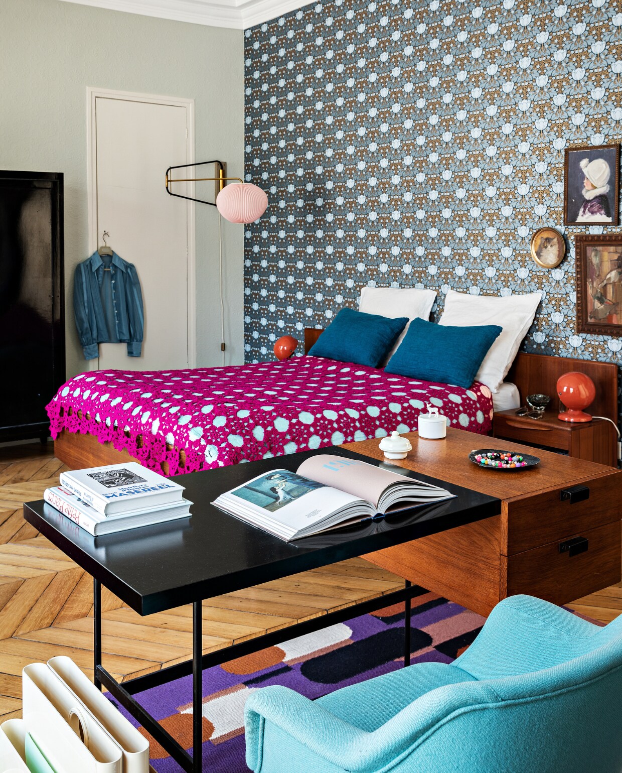 Behang Etoffe. Kast, bed, roze wandlamp, crochet-sprei, Pantone-bedlampen en Pierre Paulin-bureau vintage (o.a. via Selency.fr en vlooienmarkten). Vloerkleed Oman Élitis. vtwonen special binnenkijken 03-2022 | productie AC Scoffoni | styling Marie-Maud Levron | fotografie Yann Deret