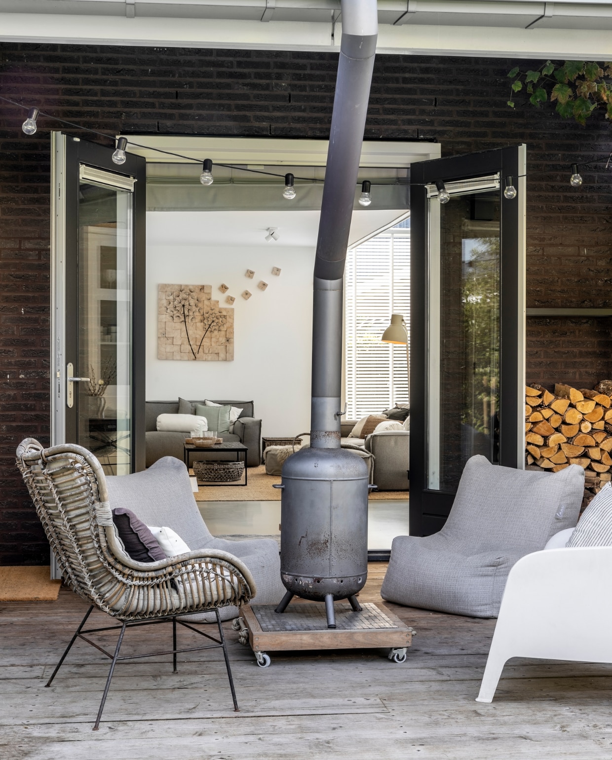 Lampensnoer Ikea, kachel Burnies, wielplateau gemaakt door Tim to Build, rieten stoel Karwei, kussen met stip Winkeltje van Anne, ander kussen H&amp;M Home, lage fauteuils Laui lounge, stoel rechts Ikea, houtrek bol.com, vlonders onbehandeld douglas. vtwonen 08-2022 | productie Cocofeatures |  fotografie Denise Zwijnen