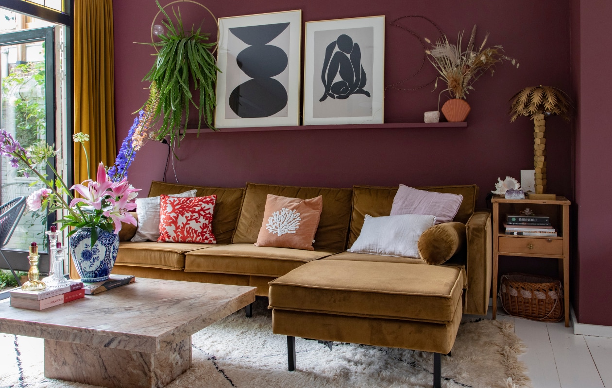 Muurverf Merlot Mania no. 123 Powderbox van Vestingh. Bank Rodeo van BePureHome, linnen kussenhoes H&amp;M Home, rode kussenhoes met schelp À La, koraalkleurige kussenhoes Leen Bakker, vloerkleed Beni Ouarain Outlet. Wandplank Ikea, maan zelfgemaakt, schelp Fonq, bloemen Happy Circle, palmboom HKliving, waxinelichthouder The Spirit Junkies, bijzettafel en mand vintage. Overig onbekend. vtwonen 08-2022 | productie en fotografie Anne den Haan | styling Luka Jakobs