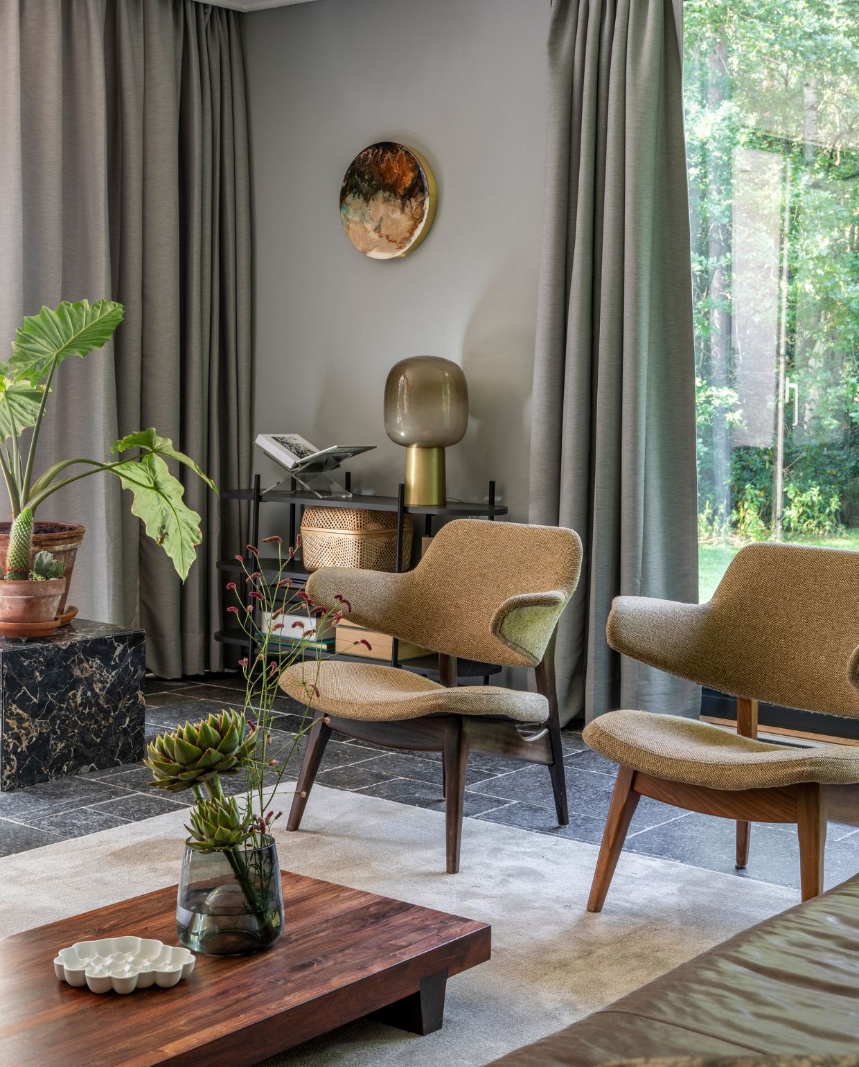 Muurverf Betongrijs Karwei. Gordijnen Ikea, vloer Belgisch hardsteen. Fauteuils vintage Louis van Teeffelen. Houten salontafel uit Japan via Catawiki, porseleinen schaal Bubble Dish van Studio Amber Isabel, glazen vaas op salontafel Loods 5. Vloerkleed Derby Beige, op maat laten maken bij Karwei. Marmeren kubus Marktplaats. Open kastje Leen Bakker, boekenstandaard Yessential, tafellamp House Doctor, opbergmand Ikea. Rond epoxykunstwerk Corine van Voorbergen. Bank Loods 5. vtwonen 07-2022 | productie CocoFeatures | styling Brenda van Roekel - Studio Amber Isabel en Lotje Deinum | fotografie Denise Zwijnen | tekst Saskia Borst