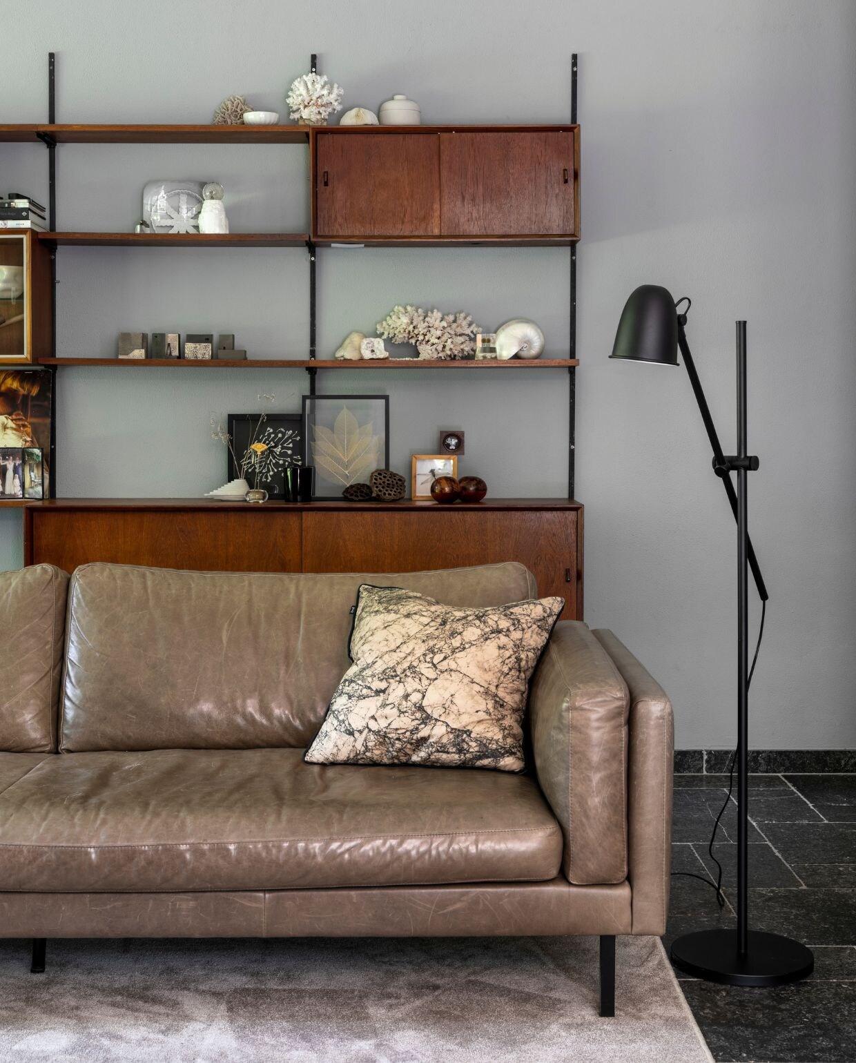 Muurverf Betongrijs Karwei. Wandkast vintage, designer onbekend. Bovenste plank: koraal vintage, wit schaaltje souvenir uit Japan, potje met deksel designer onbekend. Tweede plank: lens uit objectief voor porseleinen object van Studio Amber Isabel, stenen waxinelichthouder met paardebloem in epoxy. Derde plank: keramieken huisjes Studio Amber Isabel, koraal vintage met Nautilus parelmoerschelp. Onderste plank: betonnen vaasje en ikebana bloemhouder souvenirs uit Japan, ingelijste bloemen van porselein Studio Amber Isabel, gevonden libel ingelijst door opa, twee zaaddozen van lotussen uit Japan, zwarte tulpenvaas Pols Potten, koraal vintage, houten ronde bakjes souvenir uit Marrakech. Bank Loods 5, kussen op bank Ferm Living, zwarte lamp naast bank Ikea, vloerkleed Derby Beige Karwei. NEE | vtwonen 07-2022 | productie CocoFeatures | styling Brenda van Roekel - Studio Amber Isabel en Lotje Deinum | fotografie Denise Zwijnen | tekst Saskia Borst