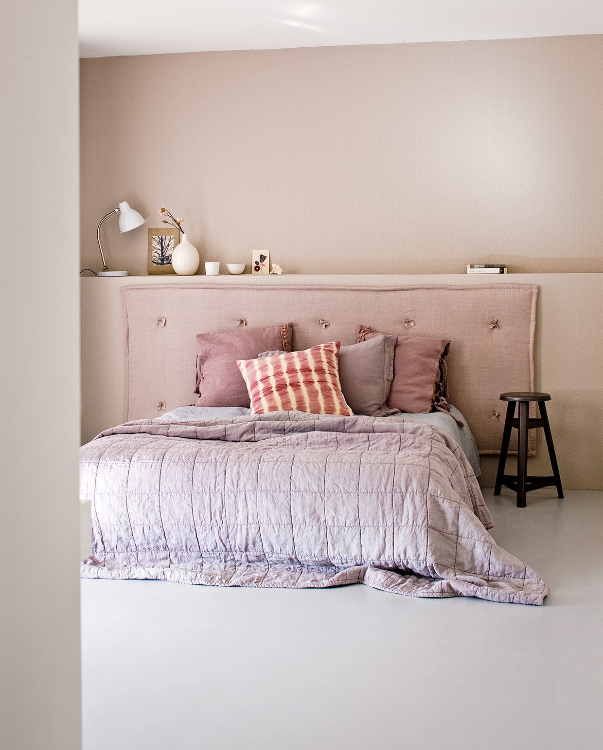 Uit de vtwonen huiscollectie: overschilderbaar behang Knitty per rol € 27,95, witte leeslamp € 299,-, roze tie-dye kussen 60×60 cm € 39,95, witte vaas € 14,95 oudroze linnen kussen met striksluiting € 44,95. Stof gebruikt voor hoofdbord Stonewashed (Chivasso). Kleur op behang: Elephant’s Breath (Farrow &amp; Ball). Overig privébezit JA | vtwonen 02-2013 | styling Cleo Scheulderman | fotografie Jeroen van der Spek