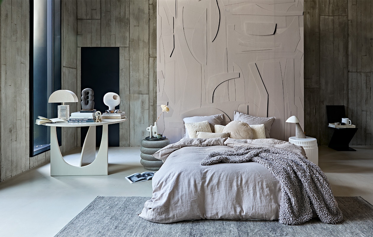 Behang op roomdivider White Spirit, op maat geprint, prijs op aanvraag (pascale-risbourg.com). Taupe-kleurig linnen beddengoed, 220×240 cm € 99,-, plaid van imitatie schapenvacht, 110×150 cm € 69,99 (hm.com). Grijze poef van Ferm Living, 42×40 cm (Øxh) € 679,- (edha-interieur.nl). Keramieken bijzettafel Kolos van Mini Forms, 45×46 cm (Øxh) € 1325,-, vloerkleed Lavo van Kvadrat, 300×200 cm € 2208,-(kasstoor.nl). Zwarte vintage zigzagstoel van Rietveld, prijs op aanvraag (vintage­hoarder.com). Tafel 120×75 cm (Øxh) vanaf € 750,- (com-anders.nl). Vaas met gat op de stapel boeken € 39,95, teddy kussen 30×80 cm € 49,95, teddy kussen 40×40 cm € 29,95 (urbannatureculture.nl). Bruine sculptuur Guaja van klei, 18x8x33 cm (bxdxh) € 450,-, kleine stenen sculptuur Kisii Stone op tafel € 25,- (studio-yen.com). Links op grote tafel tafellamp Hexagon L, kap € 72,95, marmeren voet € 149,95 (hkliving.nl). Sculpturale vaas van ontwerper Jonathan Adler naast bed, € 209,- (ankevangoor.com). Klein linnen kussen, 30×50 cm € 15,99 (zarahome.com). Dienblad vanaf € 69,- (luxurybynature.nl). Keramieken waterkan van ontwerper Vincent van Duysen van Serax € 25,- (vtwonen.nl). Tafellamp Fellow met marmeren voet rechts naast het bed van Fredericia € 864,- (designtales.nl). Wandbekleding van locatie. Overig privébezit. vtwonen 02-2021 | styling Cleo Scheulderman | fotografie Jeroen van der Spek