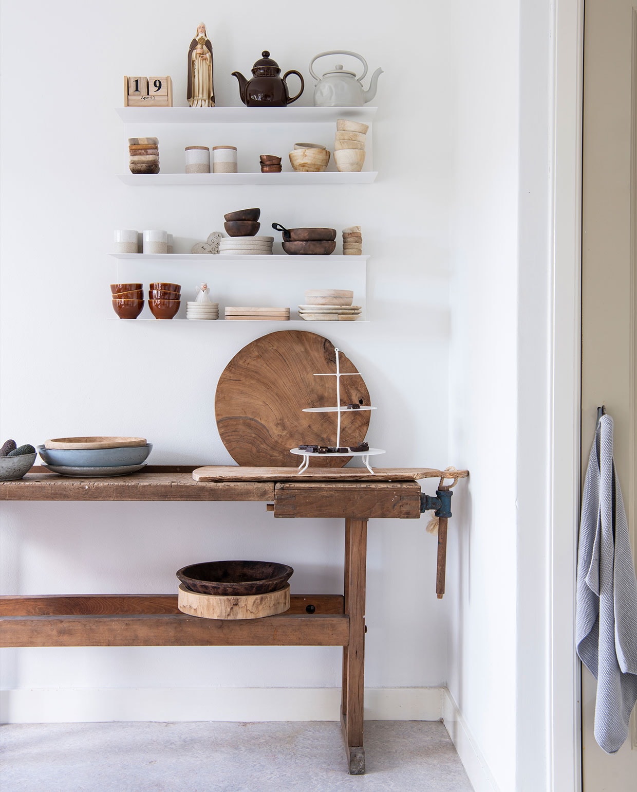 Wandplanken Ikea. Op de planken, van links naar rechts en boven naar beneden: kalender Twee21, beeld cadeau, bruine theepot Tablejoy, grijze theepot Kastanje Wonen, houten bakjes kringloopwinkel, voorraadpotten en aardewerken kommen Bloomingville, houten kommen Anne-Marie Wonen, kopjes en borden Bloomingville, houten kommen NADesign, geglazuurde kommen Tablejoy, bordjes Bloomingville, plankjes Anne-Marie Wonen, aardewerken borden en kom Bloomingville. Werkbank herkomst onbekend. Vijzel Passie Wonen Soest. Blauw-grijze schaal en grijs bord Broste Copenhagen via Twee21. Diverse houten kommen en snijplanken Anne-Marie Wonen. Etagère K’willeminhuis. Theedoek Södahl. vtwonen binnenkijk special 121-2021 | productie Insidehomepage | styling Esther Loonstijn | fotografie Louis Lemaire