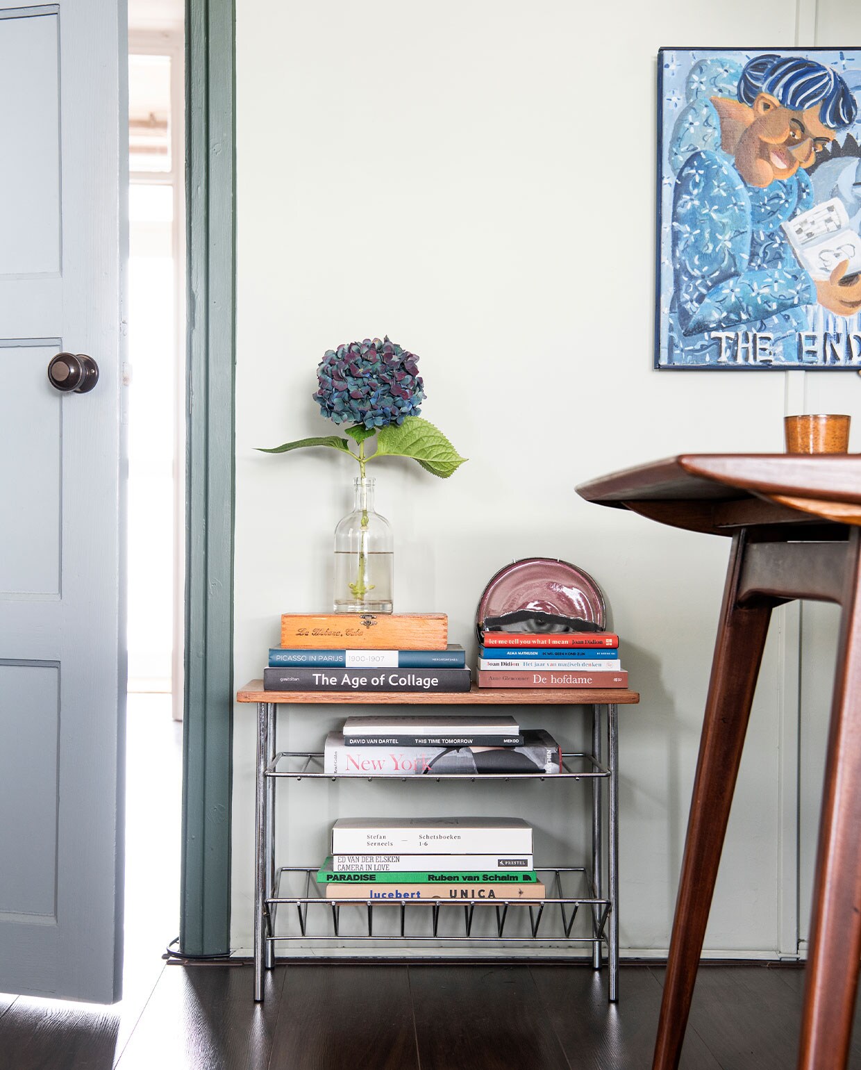 Tijdschriftenrek erfstuk, fles Vørding’s Gin, bord van Vivian Hann, tafel vintage, kunst van Ralf Kokke. Overig onbekend. NEE | vtwonen 6-2022 productie Insidehomepage | styling Kim Timmerman | fotografie Louis Lemaire  | tekst Anne-Flore Muller