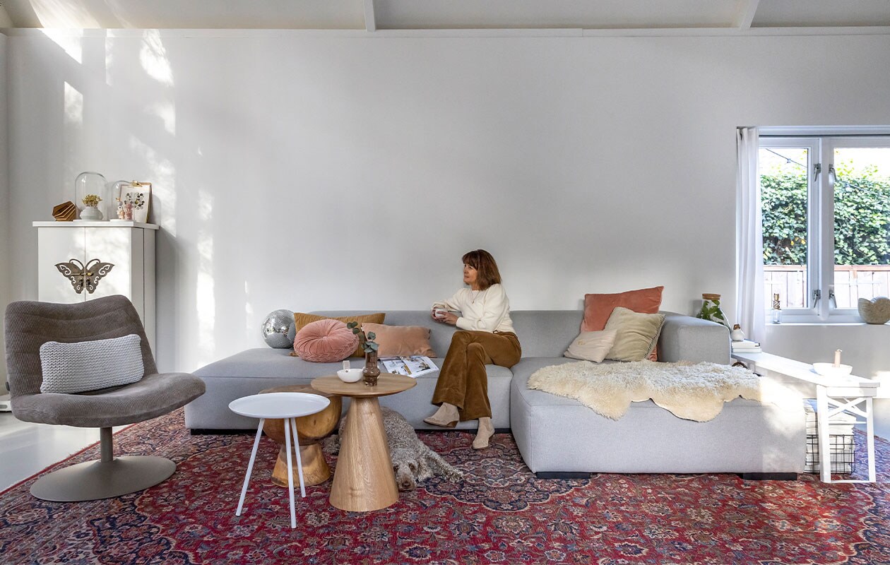 Bank Koozo, geel kussen en gordijnen Ikea, rond kussen en kandelaar in vensterbank Loods 5, lichtroze kussen Sissy-Boy, roze kussen rechts Dutch Decor, zandkleurig kussen Atelier Pomme, lichtgroen kussen, grote houten tafel, draadstaalmand en discobal Kwantum, kleine houten tafel Marktplaats, witte tafel Zuiver, schapenvacht Zalando Lounge, kleed overgenomen van vorige bewoners, vlinderkast Het Kabinet, muur ral 9016, stoel Zuiver, kussen in stoel Goround interior, grote stolp Mica Decorations, vaas Hella Duijs, kleine stolp Hema, pop in stolp links Lammers&amp;Lammers, pop rechts atelier W, lamp Tjalle en Jasper, klembord Hema, poster Jurianne Matter, witte schaal Jet at Home, vaas Huizedop via Kruidvat, biertafel herkomst onbekend, kandelaar Storefactory, plant in glazen fles cadeau gekregen. NEE | vtwonen 4-2022 | fotografie Henny van Belkom | tekst Martine de hoog
