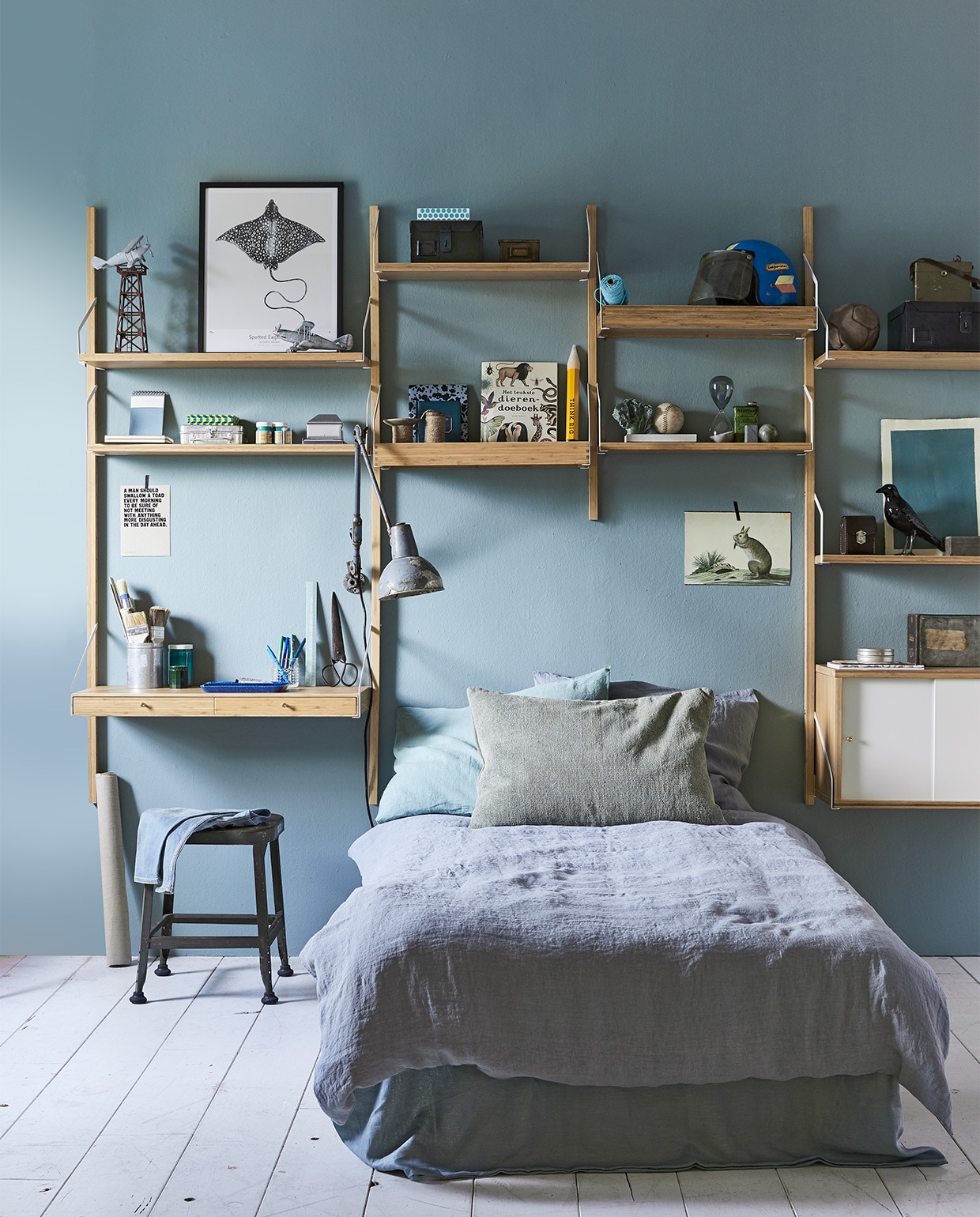 Kastenwand van wandkastensysteem Svalnäs, zoals hier afgebeeld € 344,- (Ikea). Op de muur muurverf in kleur Oval Room Blue 85 van Farrow &amp; Ball per liter € 42,- (De Ru). In de kast: helm € 30,-, leren bal € 55,-, vintage vliegtuigen € 15,-, oude miniatuur spoorwegonderdelen € 20,-, kruk Lyon Barstools € 145,-, bureaulamp € 120,- (Spoor 38). Dierenboek € 10,-, XL potlood € 8,95, zwarte kraai € 59,95 (&amp;Klevering). Metalen opbergdoos klein € 39,-, groot € 49,- van Home Industrials (Brût Amsterdam). Aluminium kistje € 19,50, lage blauwe pennenbak € 19,-, lichtblauwe liniaal € 9,90, spelletjesdoos € 20,-, lichtblauwe notitieboekjes € 16,50 (Six and Sons). Zilverkleurige perforator € 29,50, zandloper vanaf € 12,-, blauwe pennen vanaf € 3,- (Hay Amsterdam). Gevlekt schrift van Els &amp; Nel € 12,50, afbeelding vis Spotted Eagle Ray, 40×50 cm zonder lijst € 39,50 (My Deer Art Shop). Op bed: groen kussen, 70×50 cm € 58,50 (De Weldaad). Blauw linnen dekbedovertrek Blue Grey, 140×200 cm € 199,-, kussensloop € 35,- (Couleur Locale). Overig privébezit. JA | vtwonen 10-2017 | styling Cleo Scheulderman | fotografie Jeroen van der Spek