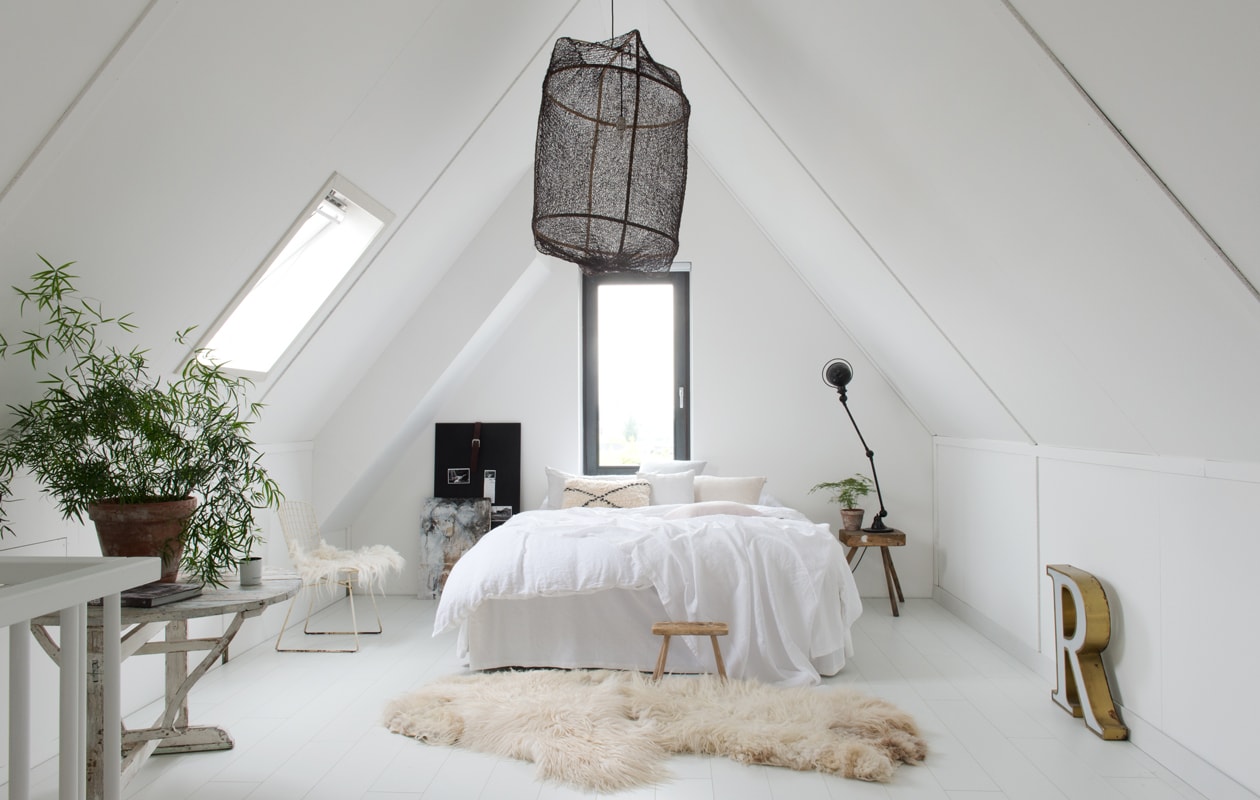 De ouderslaapkamer is licht en wit en ingericht met veel vintage. Hanglamp Ay lluminate. Bertoia Chair met vilten vacht van Marktplaats. Voor het bed vilten schapenvacht, Marktplaats. Houten krukje Van Hees Design. Kussen bed Souks. Bedlinnen By Molle. Zwarte lamp Jieldé. Vintage krukje als nachtkastje. Krijtbord vtwonen. Links: oude wijnklaptafel Park99. Vintage lichtletter van rommelmarkt. vtwonen 12 binnenkijken special 2019 | Styling Wilma Custers (Features &amp; More), Rozmeen Koornneef | Fotografie Trui Heinhuis