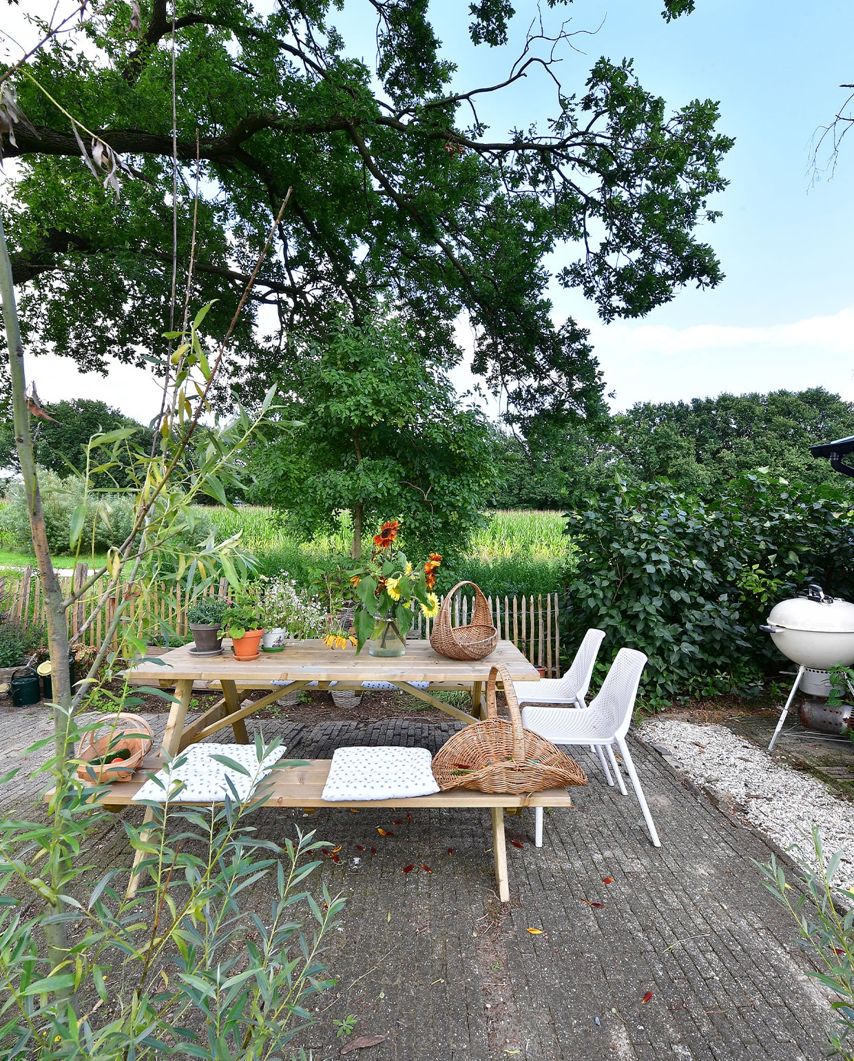 Strategisch ingericht in de schaduw van een eik: het terras. Een lekkere plek om te eten, maar ook om de plukboeketten te maken. Picknicktafel Karwei, barbecue Weber, stoelen gekregen, plukmanden kringloopwinkel, kussens Søstrene Grene. NEE | vtwonen TUIN special 5 | fotografie Sietske de Vries | tekst Monique van der Pauw