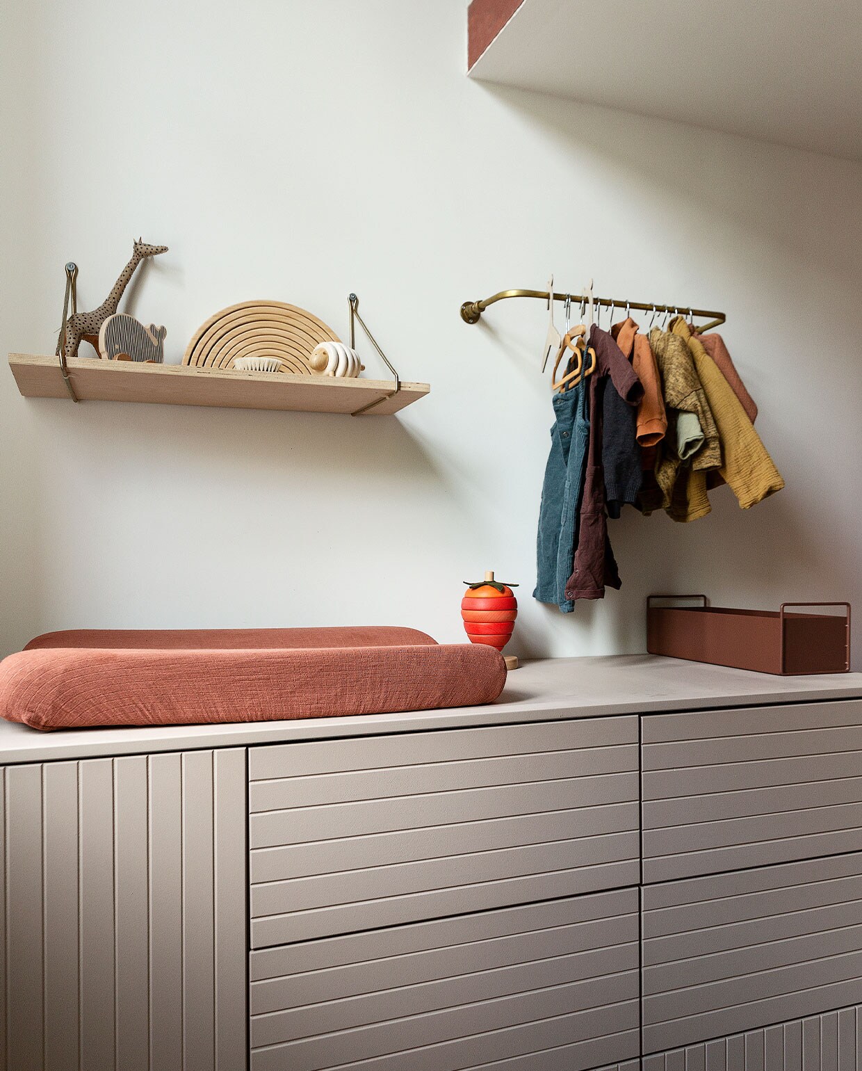 Commode eigen ontwerp op basis van keukenkasten Ikea, lijnen zelf erin gefreesd. Aankleedkussen Garbo &amp; Friends, aardbei-stapeltoren Konges Sløjd, metalen bak Ferm Living. Wandplank House Doctor, met v.l.n.r. leren giraffe uit Marrakech, walvis cadeau, regenboog Grimm, schaap Dille &amp; Kamille, haarborstel Atelier An.nur. Messing wandrek eigen ontwerp. Vloer Marmoleum van Forbo. Muurverf Pure Sienna van Flexa. vtwonen 06-2022 | productie Martine Benjamins | styling Emmy van Dantzig | fotografie Jansje Klazinga
