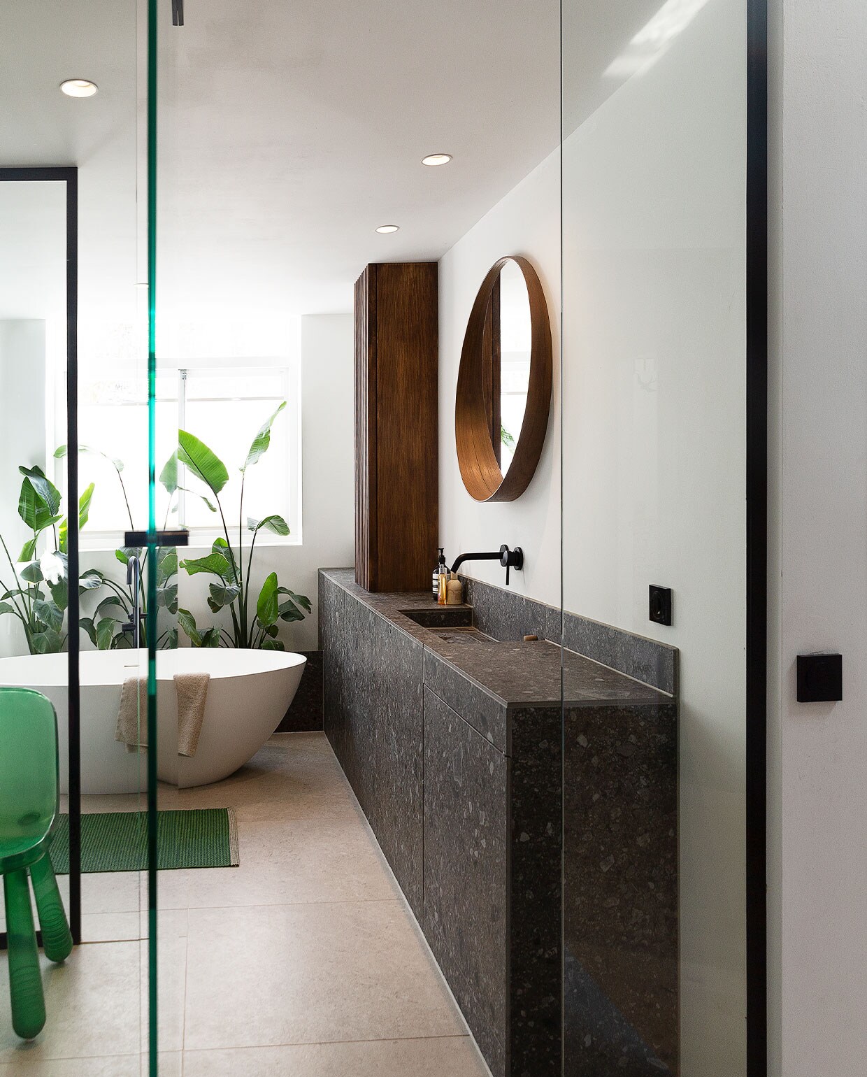 Wastafelmeubel eigen ontwerp, gemaakt van Ceppo di Gré Anthracite van Marazzi. Kraan en badkuip inclusief kraan Best Design. Spiegel Ikea. Hoge smalle walnoot­fineer kast eigen ontwerp. Stoel van Marcel Wanders via Moooi. Badmat Pappelina. Handdoek Zara Home, planten Ikea. Lichtknoppen Berker. Tegelvloer Marazzi, type onbekend. Muurverf Ral 9016 van Fairf. Overig herkomst onbekend. vtwonen 06-2022 | productie Martine Benjamins | styling Emmy van Dantzig | fotografie Jansje Klazinga