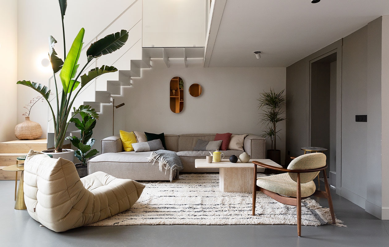 Metalen trap eigen ontwerp. Bank Dunbar van Fést, fauteuil Togo van Ligne Roset, stoel Roundy en serviesgoed Pols Potten, vintage salontafel via Marktplaats. Kleed Beni Ouarain uit Marrakech, spiegels Serax, plaid Evenaar. Ronde aardewerken vaas Pottery Pots, plantenbakken Ferm Living, planten Intratuin en 123planten. Messing bijzettafel HKliving, bijzettafel op hoge poten Pols Potten. Kussens HKliving en Pols Potten. Staande leeslamp Karwei. Plafondspots Spyder van Wever &amp; Ducré. Egalinevloer 2-componenten. Muurverf Ral 7030 van Fairf. Overig herkomst onbekend. vtwonen 06-2022 | productie Martine Benjamins | styling Emmy van Dantzig | fotografie Jansje Klazinga