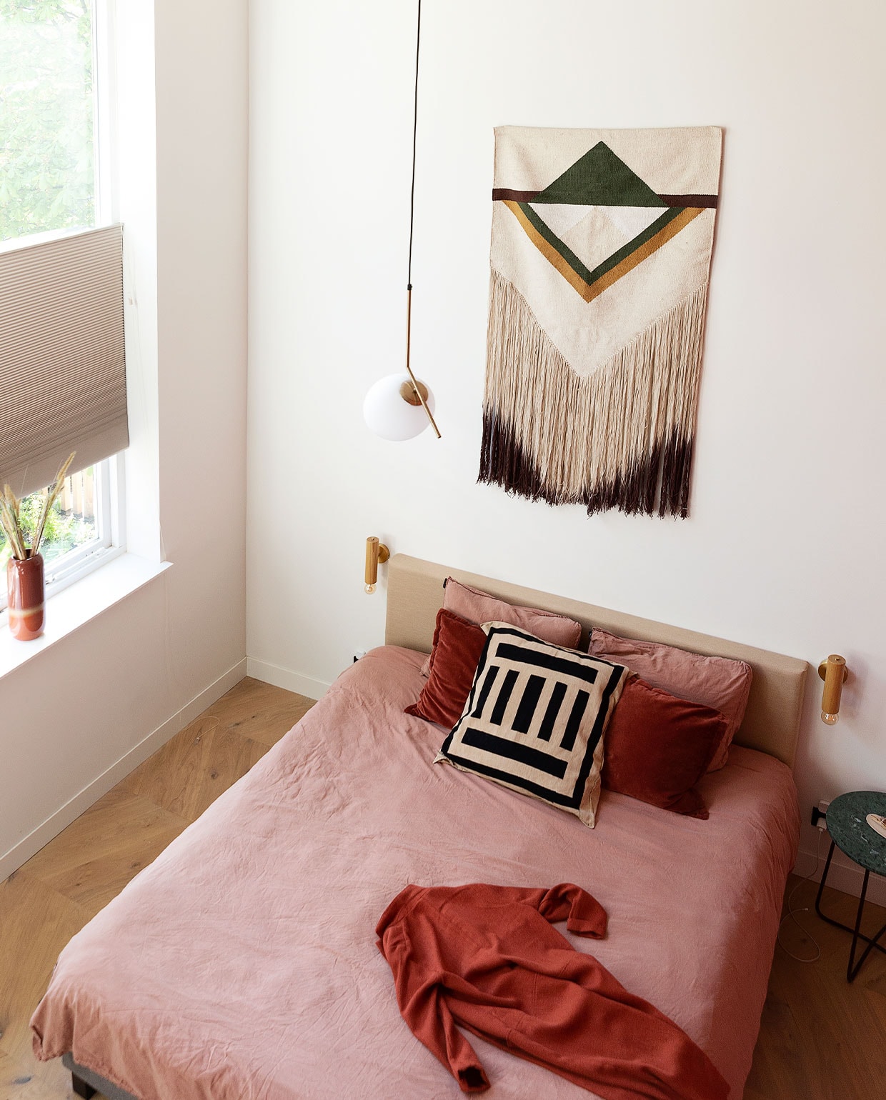 Bed Wehkamp, beddengoed La Redoute, bordeauxrode kussens Tica, gestreept kussen uit Zuid-Afrika. Ochtendjas H&amp;M. Bedlamp AliExpress, wandkleed HKliving. Hanglamp Ic Lights van Flos. Bijzettafel Dutchbone, vaas Tica, raambekleding in kleur Latte van Veneta. Eikenhouten vloer in Hongaarse punt. Muurverf kleur Leonie van Fairf. vtwonen 06-2022 | productie Martine Benjamins | styling Emmy van Dantzig | fotografie Jansje Klazinga