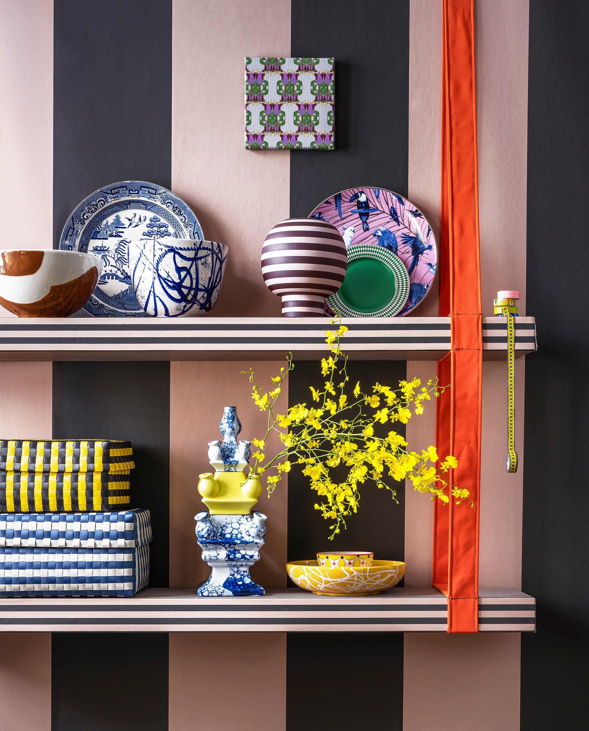 Planken met ophangsysteem van oranje band van Combitex, prijs op aanvraag (com-anders.nl). Roze-groen streepbehang Thick Lines van Ferm Living, per rol € 79,- (misterdesign.nl). Onderste plank: opbergdozen van gevlochten kunststof vanaf € 49,- (hay.nl), 3-delige vaas € 236,- (heinendelftsblauw.nl), gele schaal met spetterdessin € 49,95 (homata.fr), kommen van Pols Potten, per 4 € 53,80 (vtwonen.nl). Bovenste plank: terra en witte schaal € 49,95 en blauw-witte schaal met spetterdessin € 49,95 (homata.fr), vintage bord tegen muur € 25,- (hetgroteavontuur.nl), gestreepte vaas van Aytm € 135,- (goeds.nl), groen ontbijtbord Chess, per 4 € 82,50 (polspotten.nl), bord met vogels inclusief ophangsysteem € 39,95 (heinendelftsblauw.nl), Japanse tape vanaf € 3,- (ikigai-designbrands.com). Kunst op canvas Tulpen art deco van Iyaan, 20×20 cm € 49,- (werkaandemuur.nl). vtwonen 06-2022 | styling Marianne Luning | fotografie Stan Koolen