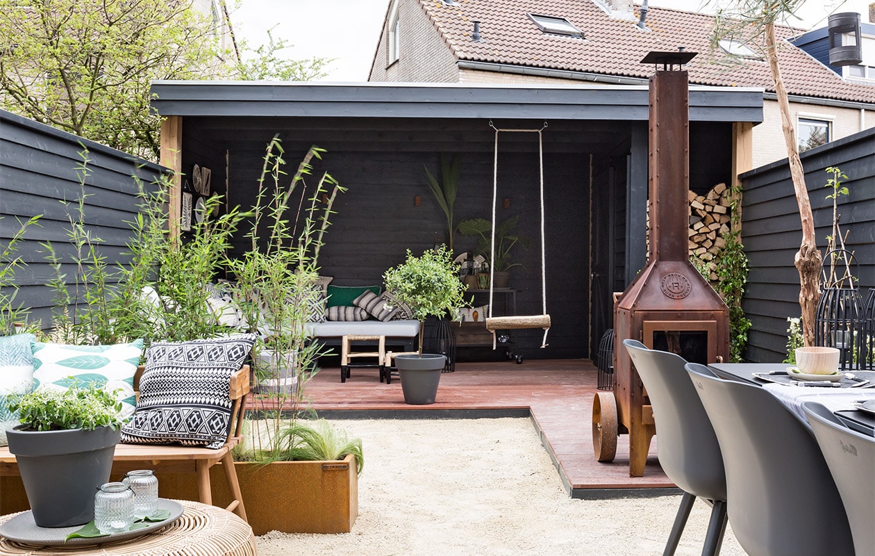 Schutting, buitenkamer op maat gemaakt, vlonderplanken en veranda, prijs op aanvraag (jandeboertuinhuizen.nl). Borderbakken van cortenstaal, op maat gemaakt, prijs op aanvraag, (blumeta.nl). Lampen Ace down cortenstaal finish, € 121,- (in-lite.nl). Poster van HK Living € 12,95, bord walvis van Magpie € 34,95, krukjes van HK Living, set van 2 € 68,-  (vtwonen.nl/shop). Bord € 1,- (kringloop). Hout met raafprint € 24,95, boomschijfje met veerprint € 8,95 (atelier8.nl). Poef € 95,- (www.kleurmeester.nl). Bank op maat gemaakt, prijs op aanvraag (jandeboertuinhuizen.nl). Zitkussens op maat gemaakt van outdoor stof, per m² € 30,-, kussen prijs op aanvraag (kleurmeester.nl). Plaid van Malagoon, 125x250 cm € 39,95, gestreepte kussens van Hartman, 50x50 cm € 19,95, kussens met kwastjes van Tine K Home, 40x60 cm € 33,95, kussens met zigzagprint van Tine K Home, 60x60 cm € 37,99, groen-wit kussen van HK Living € 34,95, grijs kussen Fox van Hartman, 50x50 cm € 22,95, kussen Plumes met veertjes van Hartman, 50x50 cm € 22,95, kussens Indi van House Doctor € 32,99, groen mohair kussen van Lifestyle, 50x50 cm € 39,95, zwart-wit kussen met varen van HK Living € 19,95 (www.vtwonen.nl/shop). vtwonen weer verliefd op je huis, seizoen 6, aflevering 12 | styling Leonie Mooren | fotografie Barbara Kieboom