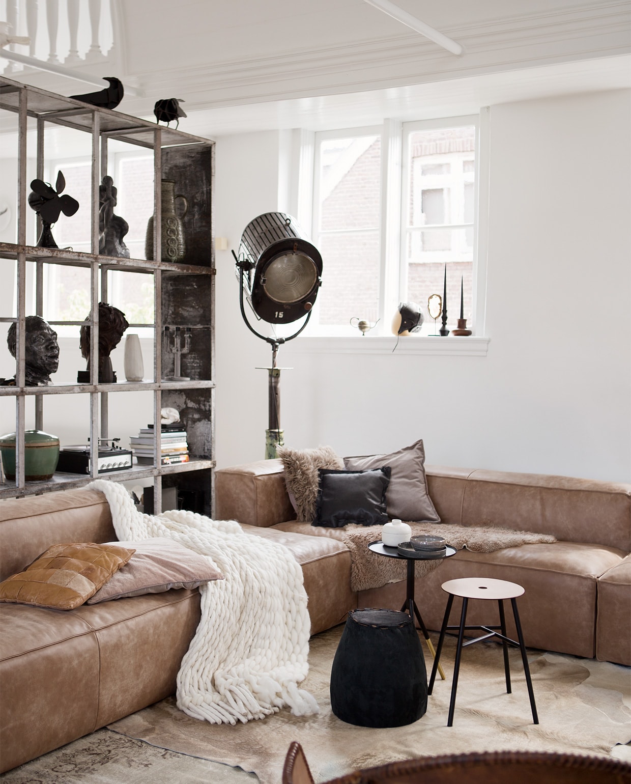 Bank Urban Loft Sofa, hier met 2x2,5 zits met een arm 177x70x96 cm per stuk € 1710,-, grote hocker 95x40x95 cm € 662,- (Raw Materials). Koeienhuid € 125,- (Puur Leer). Vloerkleed zand, 283x170 cm € 590,- (www.rozenkelim.nl). Zwarte bronzen bijzettafel van Dutchbone, 37x59 cm (Øxh) € 89,-, kruk met leren zitting van House Doctor € 54,99, matzwarte kandelaar van House Doctor, hoogte 18,5 cm € 25,99 (www.vtwonen.nl). Plaid Levensdeken van Texelse schapenwol, 280x140 cm € 1825,- (Ro Smit). Vloerlamp oude filmspot € 595,- (Neef Louis). Zwarte kaarsen € 6,75 (Ester &amp; Erik). Hoofd prijs op aanvraag (Six and Sons). Kussens bank, kast met inhoud en vliegenierspet privébezit. vtwonen 12-2016 | styling Leonie Mooren, Liza Wassenaar | fotografie Rolinda Windhorst