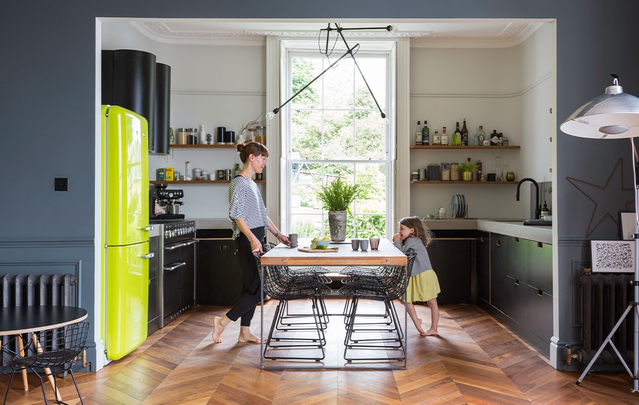 Muurverf Matt Emulsion in kleur French Grey Pale van Little Greene. Koelkast Smeg. Eettafel gemaakt van een oude kerkdeur, vintage stoelen Bertoia, kroonluchter zelfgemaakt. Keukenkasten Ikea met op maat gemaakte frontjes en deuren van Matt Antrobus, werkblad Mass Concrete, afzuigkap CDA, planken gemaakt van gebruikt hout, kraan Franke. Espressomachine Sage. Voorraadpotten Orla Kiely. Vloer Hicraft. Onderstel tafel Stone Butterfly met zelfgemaakt blad van multiplex. Overig onbekend. vtwonen 05-2022 | productie Living Inside | fotografie Kasia Fiszer