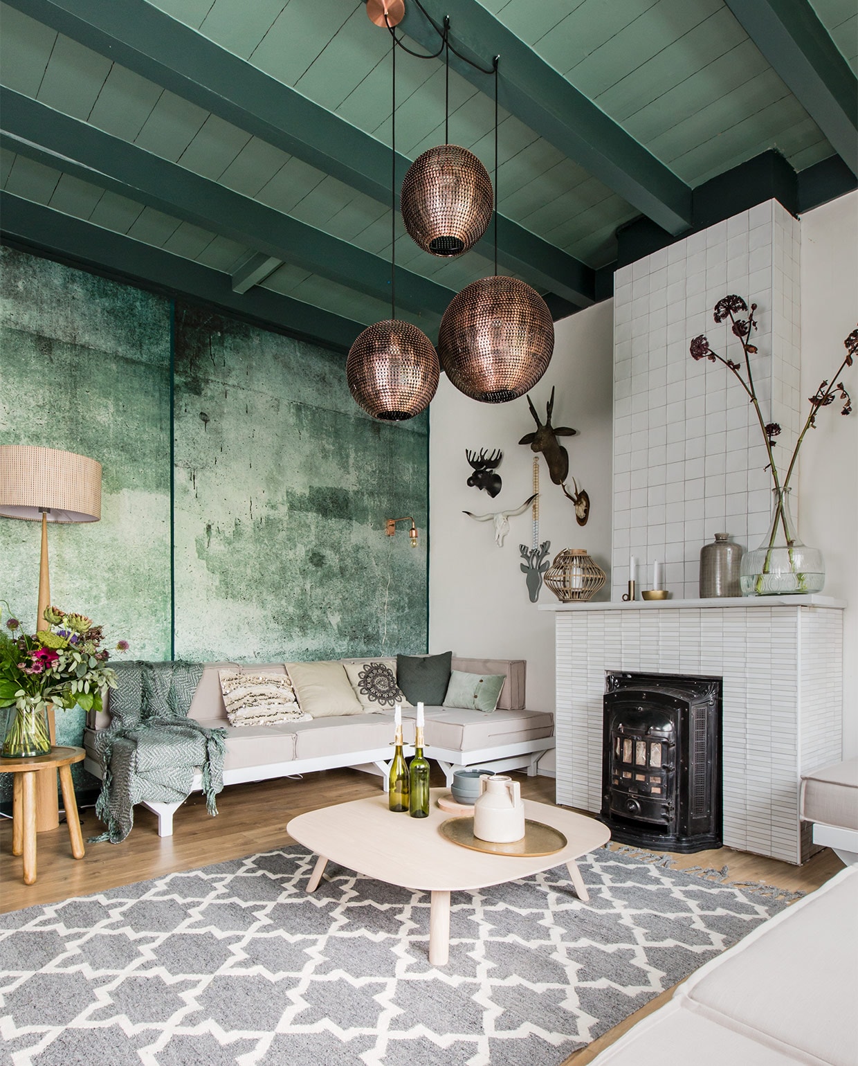 Behang Green Weathered Wall uit de collectie Resource, 4 banen, 212×280 cm (bxh) € 319,- (www.eijffinger.com). Tegels op haard: boven Square Powder wit, 10×10 cm per m² € 64,-, onder Mediterannea Javea Blanco Nieve, 20×20 cm per m² € 51,85 (www.vtwonen.nl/vtwonen-collectie). Bank op maat gemaakt, prijs op aanvraag (www.com-anders.nl). Matraskussens soortgelijk, 80×80 cm per stuk vanaf € 115,-, kussen met pailletten € 29,- (www.householdhardware.nl). Vloerkleed 170×240 cm € 299,-, salontafel Tablet, 100x100x25 cm (lxbxh) € 699,-, vloerlamp € 324,95, plaid 180×1340 cm € 64,95, kussen ecru € 29,95, met print € 22,50, groen € 24,95, lichtgroen € 34,95, koperkleurige wandlamp € 119,- (www.eijerkamp.nl). Koperkleurige hanglampen, per stuk vanaf € 119,- (www.dutchbone.com). Bijzettafel Dendon small € 89,- (www.zuiver.com). Hertenkoppen aan wand: wit (linksonder) € 129,-, groot (rechtsboven) € 49,95 (www.vtwonen.nl). Aan ketting € 44,- (www.couleurlocale.eu). Op schouw: windlicht € 29,95, kandelaars € 18,95 en € 24,95, bruine vaas € 39,95 (www.vtwonen.nl). Grote glazen vaas Field Flower € 59,- (www.zuiver.com). Op tafel: grijze pot € 49,- (www.woud.dk). Houten onderbord € 29,95, kruik met oor € 19,95 (www.vtwonen.nl). Goudkleurig dienblad € 79,95 (www.eijerkamp.nl).Overig privébezit. vtwonen weer verliefd op je huis, seizoen 5 aflevering 4 | styling Fietje Bruijn | fotografie Barbara Kieboom