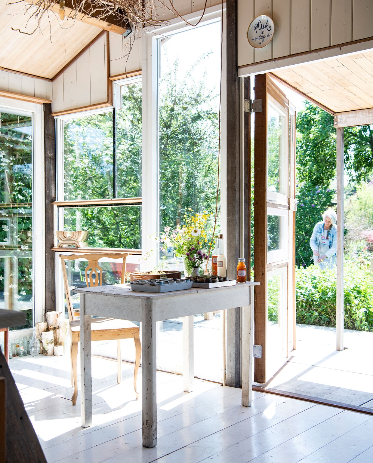 Witte vloerplanken gekregen van een vriendin, deuren en ramen gemaakt van kozijnen gevonden in containers, bord boven deur gemaakt door Simone te koop in haar webwinkel winkelgloria.nl. Tafel kofferbakverkoop Buitenhuis, stoel kringloop, bakje op tafel Old Harry’s, houten kandelaar in raam kringloop Vintage &amp; More. Flessen met zelfgemaakte vlierbloesem- en seringensiroop. Veldboeket met bloemen uit eigen tuin. vtwonen tuin special 5 | Productie Insidehomepage | Styling Myla Griese | Fotografie Louis Lemaire