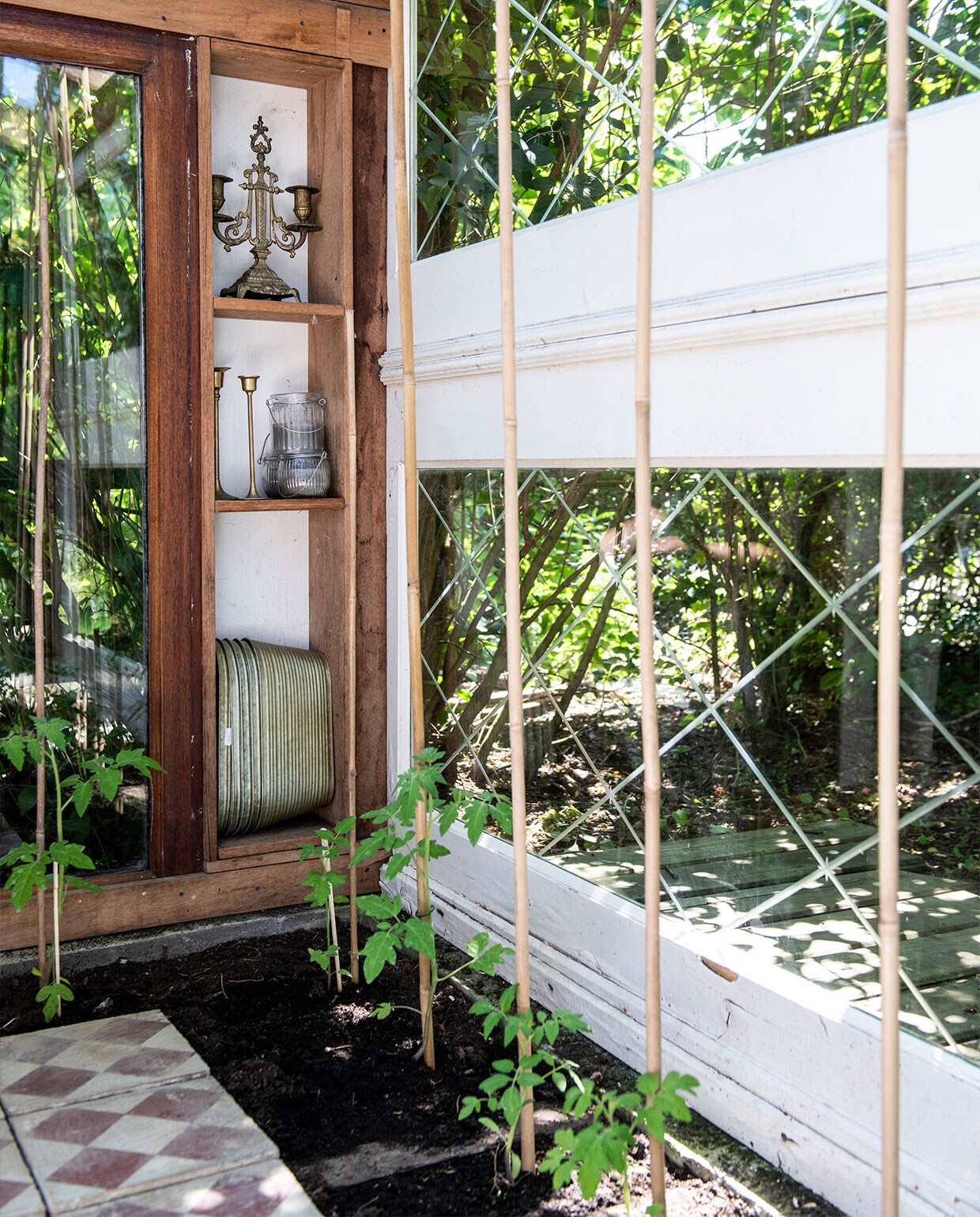 Martin maakte de kas zelf van onder andere gevonden en-suitedeuren. Kandelaren Van Manen aan Tafel, metalen plantenbakken Dickens-Style, tegels Kringloop De Driesprong Lisse. Tegen de bamboestokken groeien tomatenplanten. vtwonen tuin special 5 | Productie Insidehomepage | Styling Myla Griese | Fotografie Louis Lemaire