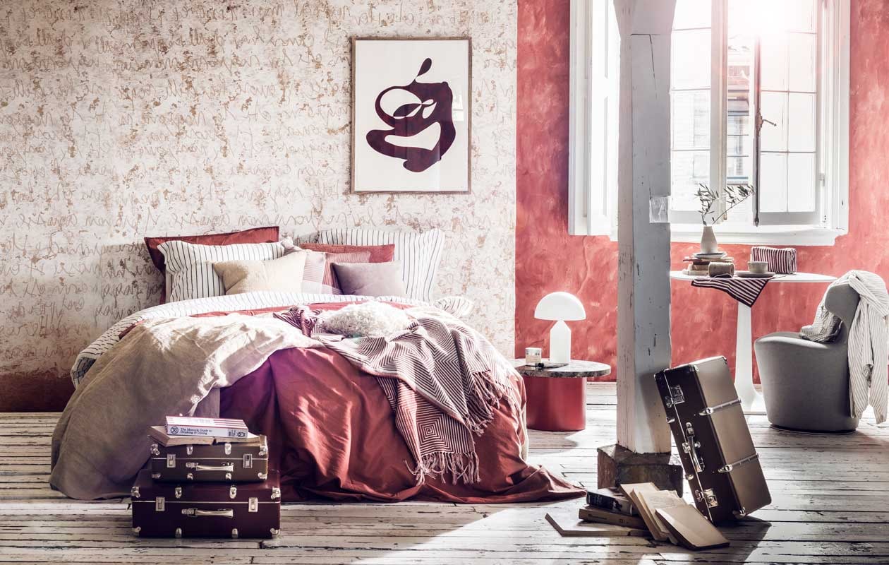 Muurverf kleur Drummond 16 van Little Greene, per liter € 43,50 (De Ru). Behang met letters, prijs op aanvraag (Wall&amp;decò). Beddengoed wit met grijze streep € 49,99, rood beddengoed € 49,99, sprei wit met rode streep 130×170 cm € 39,99, geblokte kussenhoes, 50×50 cm € 7,99, grijs-witte linnen japon € 39,99 (H&amp;M Home). Zandkleurige sprei, 130×170 cm € 89,99, kussen, 50×50 cm € 22,99 (Zara Home). Grijs kussen, 40×40 cm € 69,- (Bolia). Ronde bijzettafel Enoki gebruikt als nachtkastje € 860,-, witte lamp € 597,-(Mobilia). Toilettas rood met witte strepen € 24,95, rood-wit handdoekje op tafel € 5,95 (Anna + Nina). Witte tafel met afgeronde randen € 1386,-, grijze stoel € 1098,- (Edha interieur). Schotels per stuk € 29,-, kom € 25,-, vaasje € 35,- (Annemieke Boots Ceramics). Koffers vanaf € 45,- (Archive Store). Boek The Monocle Guide to Drinking &amp; Dining € 29,95 (Six and Sons). Kunst aan de muur € 620,- (Cate Adriana). Overig privébezit. vtwonen 07-2018 | styling Liza Wassenaar | fotografie Sjoerd Eickmans