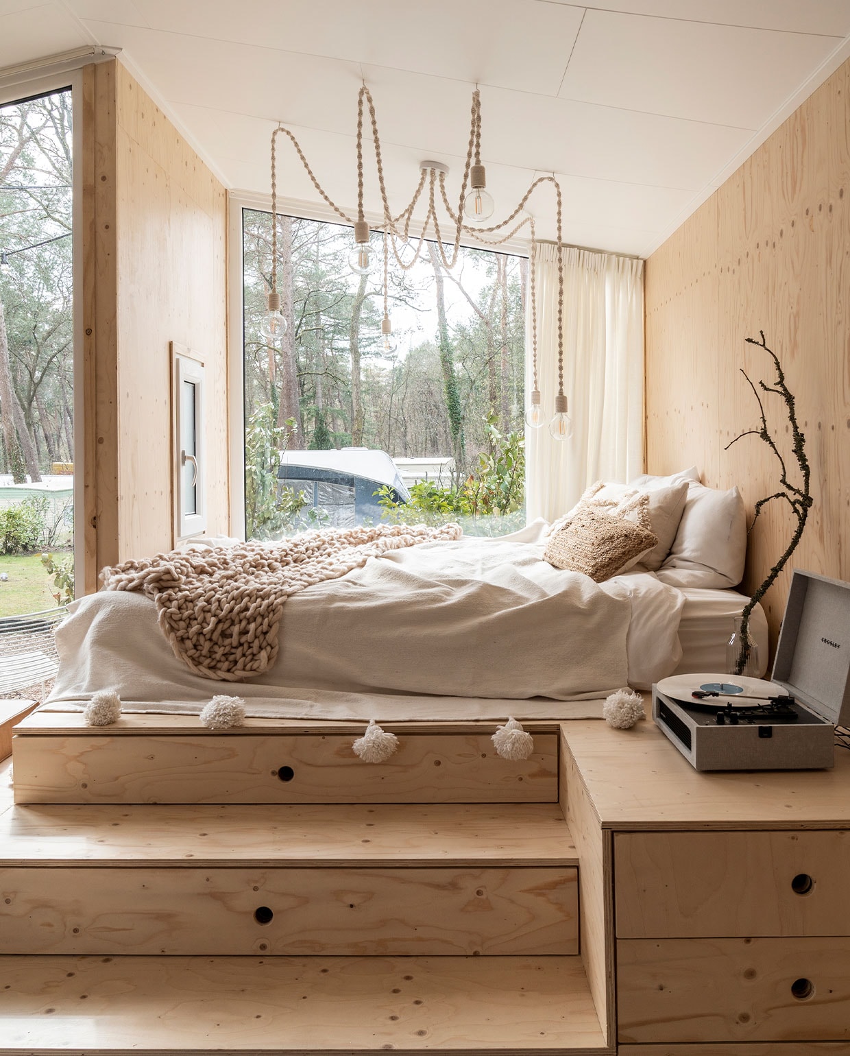 Bedombouw Hertog Recreatiebouw.Kandelaarlamp zelf­gemaakt. Matras Emma, beddengoed herkomst onbekend, sprei met pompons gekocht in Marrakech, gehaakte sprei Lidl. Waterkaraf Ikea, tak uit het bos, platenspeler Crosley, beige kussen H&amp;M Home, bruin kussen Calma House. vtwonen 11-2021 | Fotografie Muk van Lil | tekst Cathelijne van Wingerden