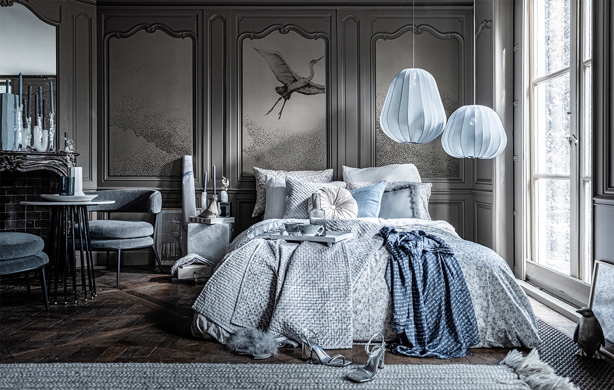 Behang op achterpaneel (wallanddeco.com). Kandelaar met takvorm van glas, witte vaas op tafel (frozenfountain.nl). Witte marmeren kandelaar met boog, blauwe en grijze kaarsen (loods5.nl). Marmeren tafeltje, wit vierkant nachtkastje, blauwe vaas,, (badenbaden.nl). Grijze stoel (edha-interieur.nl). Witte schaal op tafel groot, kleine kandelaar op schouw rechts, vaasje op nachtkastje, vloerkleed (sukha.nl). Blauwe vaas op tafel van Hay, grijze bollamp van Bolia groot, klein, zilveren pinguïn, grijze glazen , kan van Ferm Living, transparant glas naast bed van Ferm Living (vtwonen.nl). Zilveren hakken, boek op nachtkastje Noma, donkergrijs boek op de grond Christian Dior, wit linnen dekbedovertrek, rond kussen op bed, zilveren doosje op nachtkastje (hm.com). Blauw-wit dekbedovertrek met print, zilveren plaid, bijpassend kussen, sloffen met vachtje, grijs kussen, blauw kussen (zarahome.com). Doosje links op boek, boekjes op doosje (letoile.store). Blauwe ochtendjas, wit dienblad op bed, grijs-witte mokken op bed, witte pen in vorm van veer (maisonnl.com). Kunst in lijst op de grond (tinystories.nl). Beige stoffen vogel (homestede.nl). vtwonen 02-2020 | styling Liza Wassenaar | fotografie Sjoerd Eickmans
