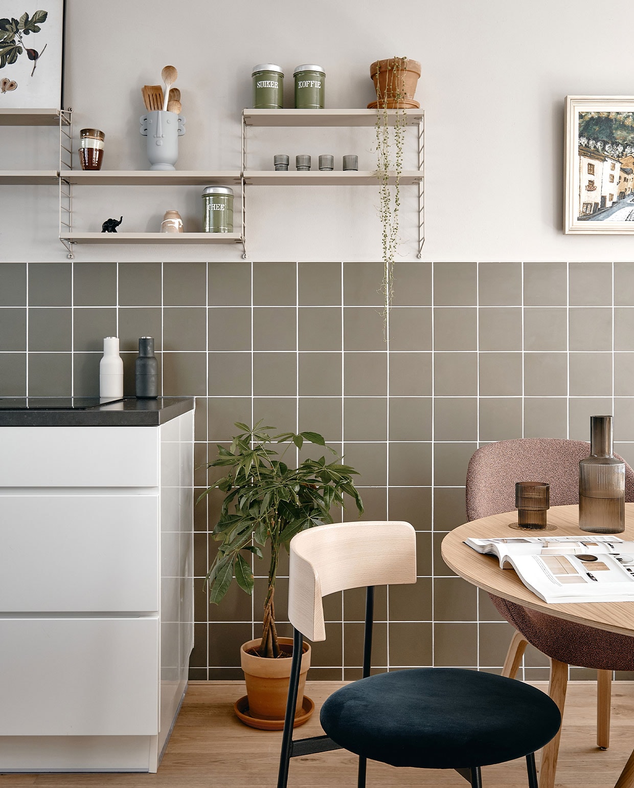 Muurverf Purbeck Stone van Farrow &amp; Ball. Wandtegels Winckelmans 15×15 cm in kleur Australian Green. Wandrek Pocket String Furniture, botanische print Junique, kopjes HKliving. Vaas cadeau gekregen. Voorraadbussen van Lindes overgrootmoeder. Peper-en-zoutstel Menu, plantenpotten Intratuin. Stoel links Friday in kleur Royal-56-petrol Fest Amsterdam. Stoel rechts About a Chair en eettafel Hay. Karaf en glazen Ripple van Ferm Living. vtwonen 05-2022 | productie Cocofeatures | fotografie Roos Oosterbroek