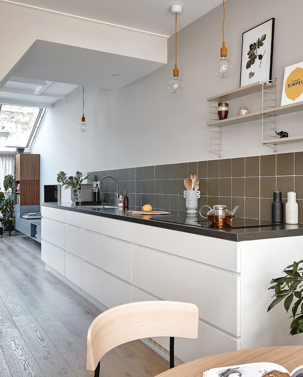 Muurverf Purbeck Stone van Farrow &amp; Ball. Wandtegels Winckelmans 15×15 cm in kleur Australian Green. Keuken Mano van Kvik met werkblad Jetstone Raven Satin van 40 mm. Hanglampen E27 Muuto. Vaas cadeau gekregen, theepot Simon Lévelt, peper-en-zoutstel Menu. Wandrek Pocket van String Furniture. vtwonen 05-2022 | productie Cocofeatures | fotografie Roos Oosterbroek