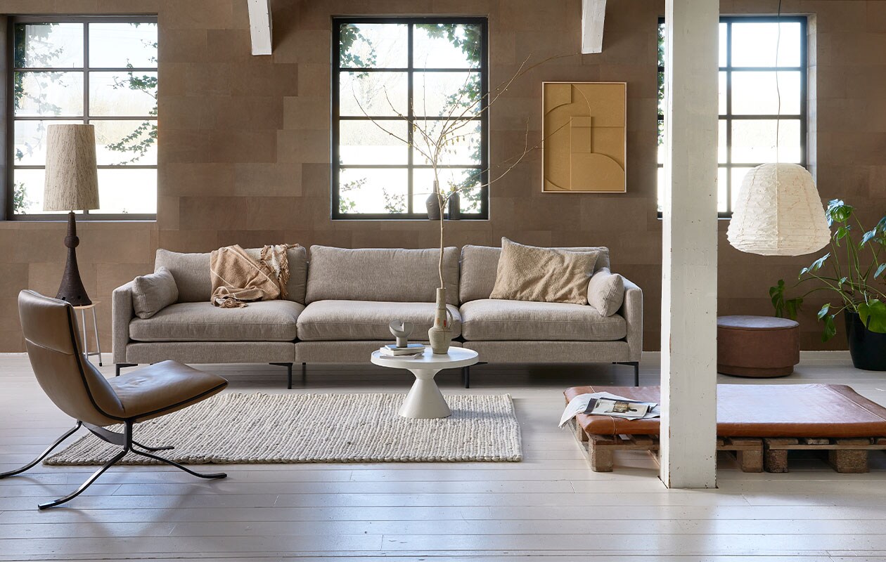 Leren wandtegels in kleur Desert, per m2 € 69,95 (enzopellini.com). Bank Summer in kleur Latte, 4,5 zits, 335 cm (b) € 2530,-, aluminium salontafel Floss, 60 cm (Ø) € 275,- (zuiver.com). Fauteuil Juno vanaf € 1549,- (eyye.nl). Handgemaakt wollen vloerkleed Hjorstvang, 160×230 cm € 349,- (ikea.nl). Leren loungemat, 100×6,5×150 cm (bxdxl) € 379,- (nahka.nl). Ecoleren poef van vtwonen in kleur Cognac, 60×36 cm (Øxh) € 159,-, plaid op bank Sahara van Malagoon, 150×125 cm € 59,95, papieren hanglamp Leena, 50×52 cm (Øxh) € 144,95, kussen, 50×70 cm € 41,90, vaasjes op vensterbank vanaf € 33,50 (vtwonen.nl). Keramische voet schemerlamp € 195,- (neeflouis.nl). Kruk € 30,- (vandijkenko.nl). Aan de wand reliefkunstpaneel in kleur Sand, 63×83 cm € 469,-, lampenkap in zijde, naturel, 36×58 cm (Øxh) € 159,- (hkliving.nl). Overig privébezit. vtwonen 05-2022 | Styling Fietje Bruijn | Fotografie Dennis Brandsma\n