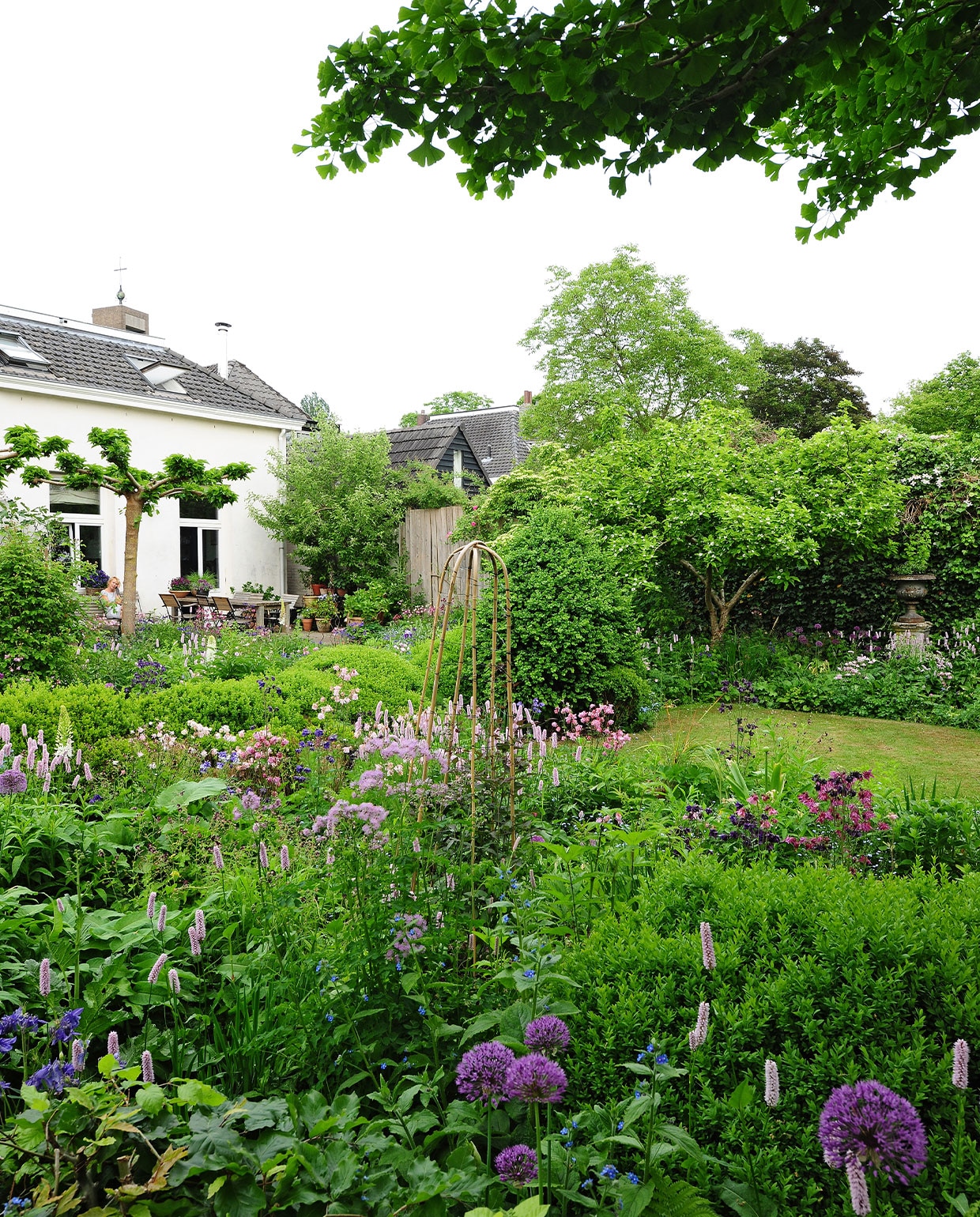 Binnen een patroon van breedbladige buxusplanten zette Miriam zo veel mogelijk bloemen neer. De betonnen sokkel met ijzeren sierpot stond al in de tuin toen ze het huis kochten. Tuintafel zelfgemaakt, herkomst stoelen onbekend. NEE | vtwonen TUIN special 04 | fotografie Sietske de Vries | tekst Eveline Stoel